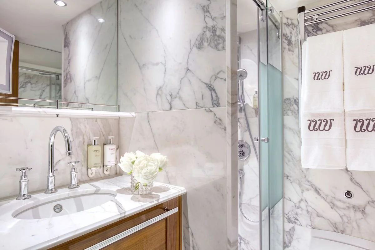 Marble bathroom with sink, mirror, towel, and shower area.