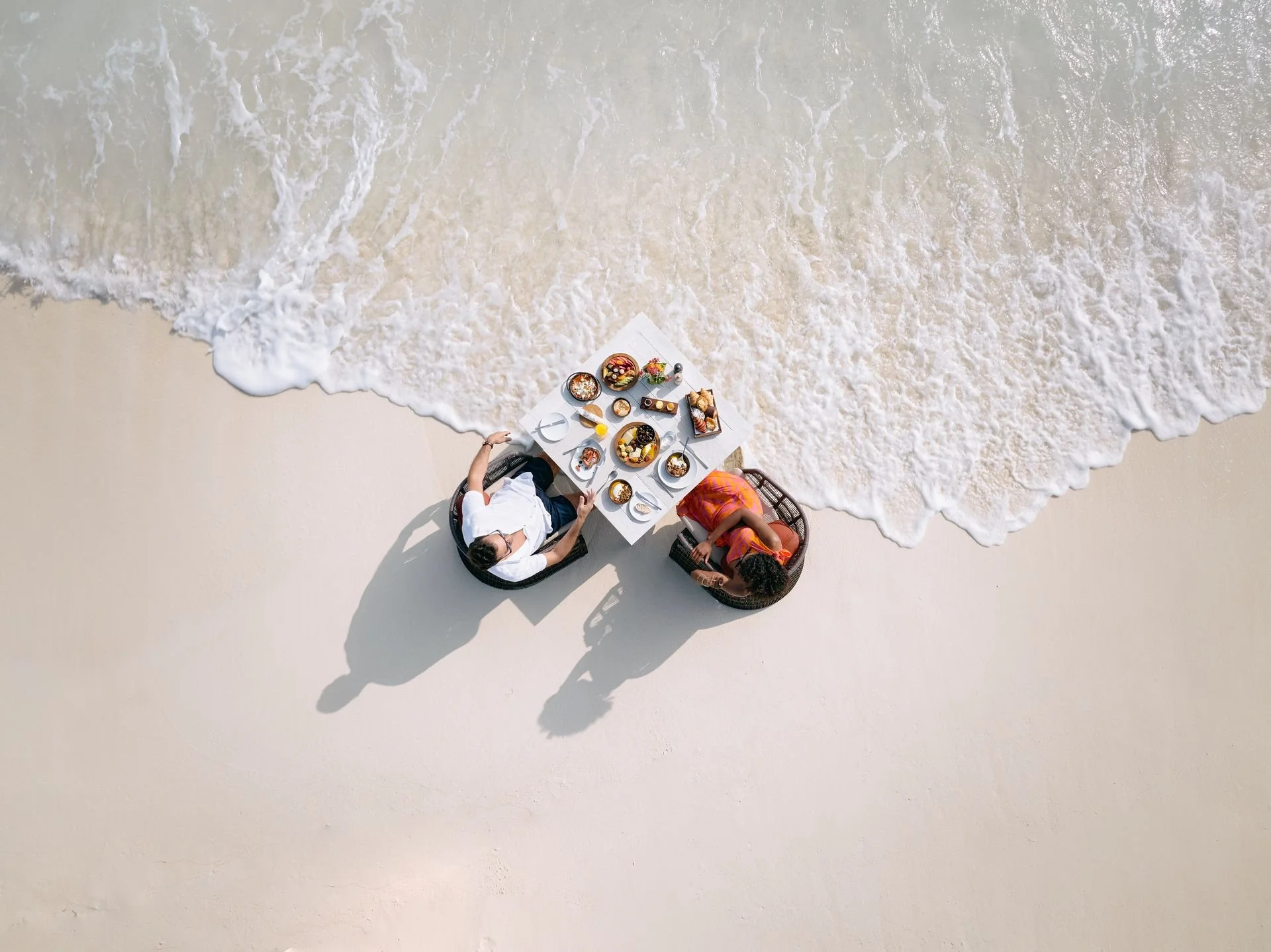 Two people enjoying a meal on a beach while waves wash onto the sand.