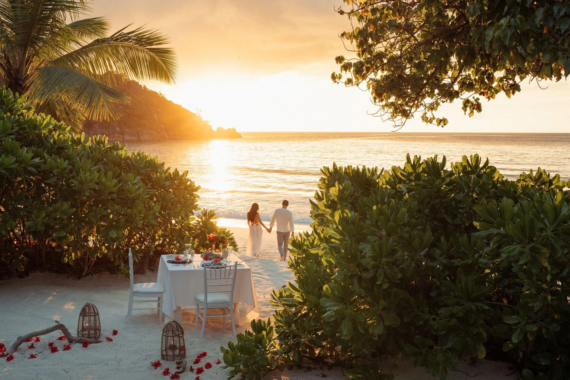 Couple holding hands walking on the beach at sunset, with palm trees and greenery framing the scene, and a table set for dinner nearby.