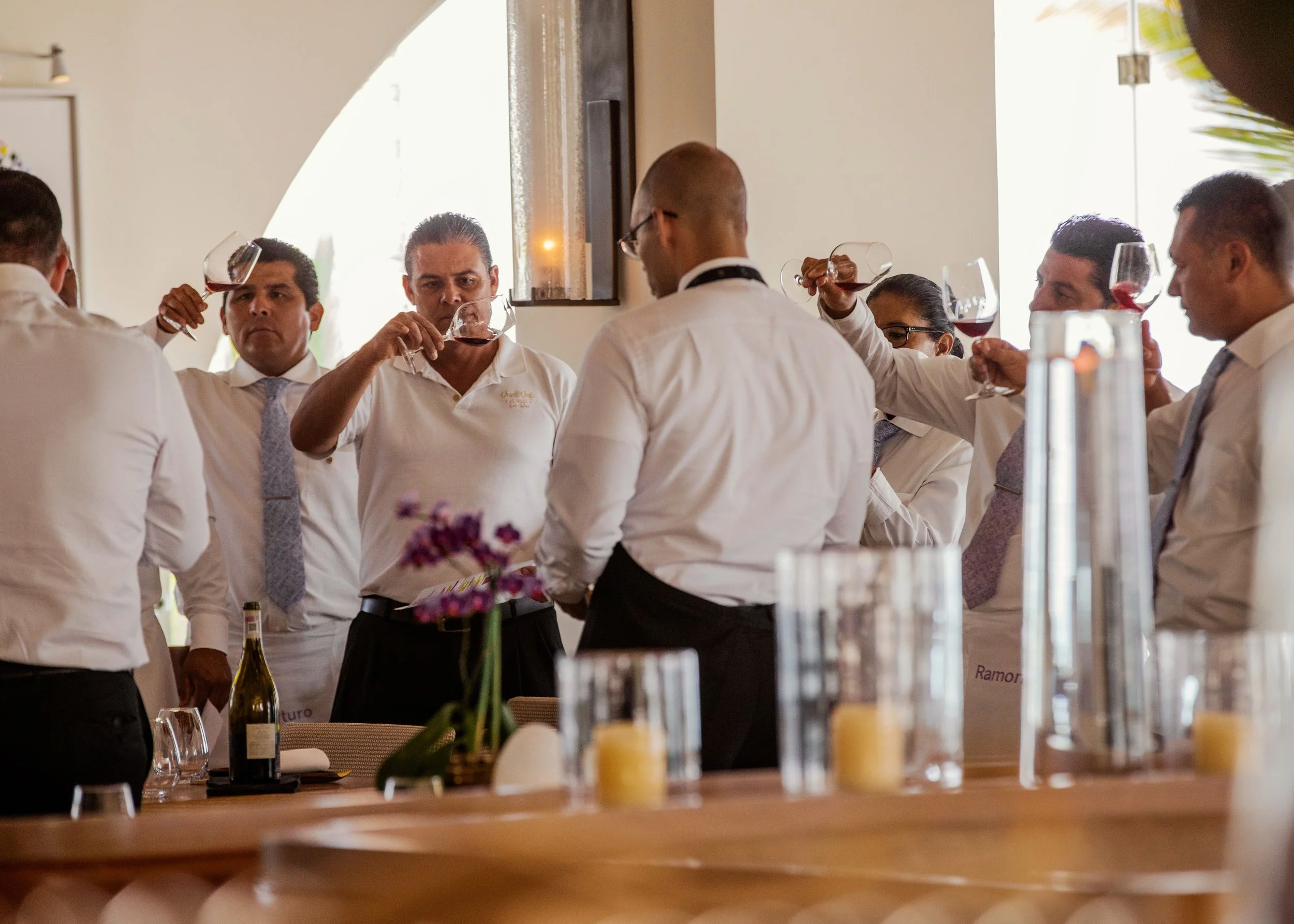 A group of people dressed in white shirts raising glasses of red wine in a toast at a restaurant or banquet setting.
