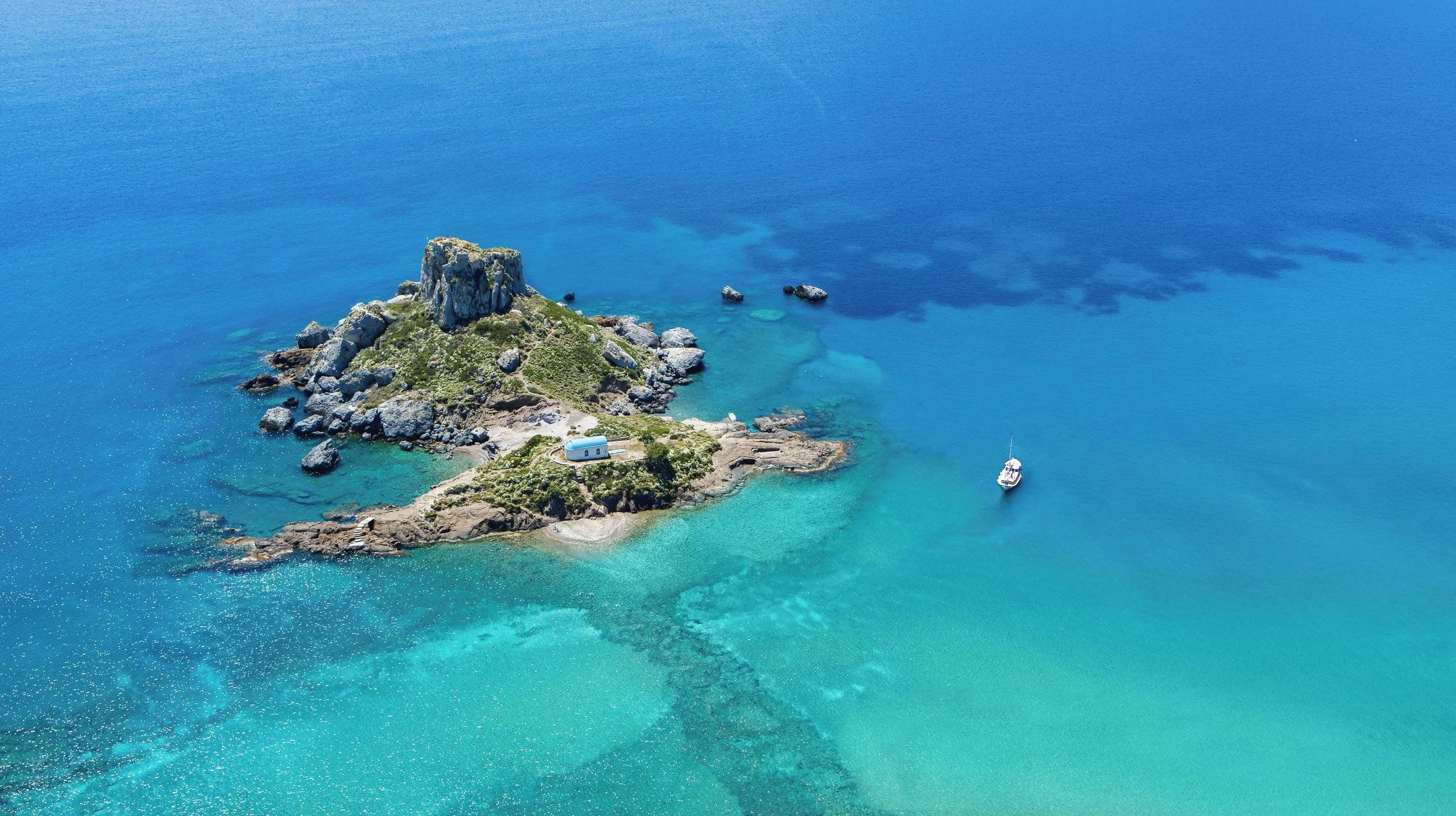 A small island with a large rock formation and a white building, surrounded by turquoise water and a boat nearby.