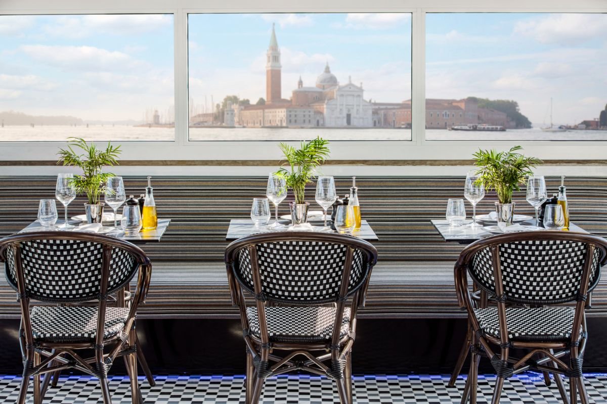 Dining table with three plants, wine glasses, and olive oil bottles, overlooking Venice with canal and historic buildings in the background