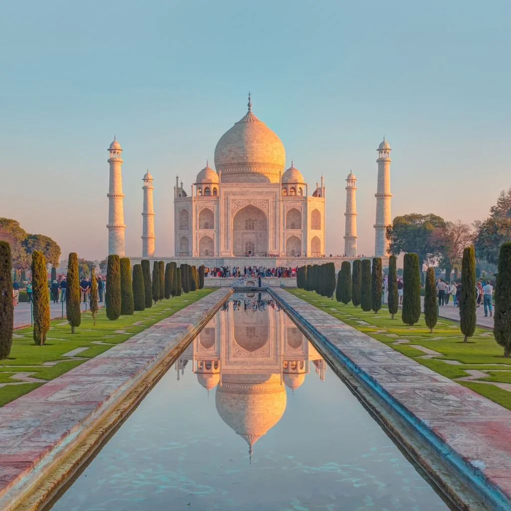 The Taj Mahal, an iconic white marble mausoleum with a large central dome and four minarets, reflecting in a long water canal flanked by green lawns and trees, with visitors in the foreground.
