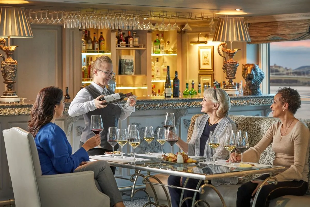 Women dining in a restaurant with a bartender pouring wine for one of them.