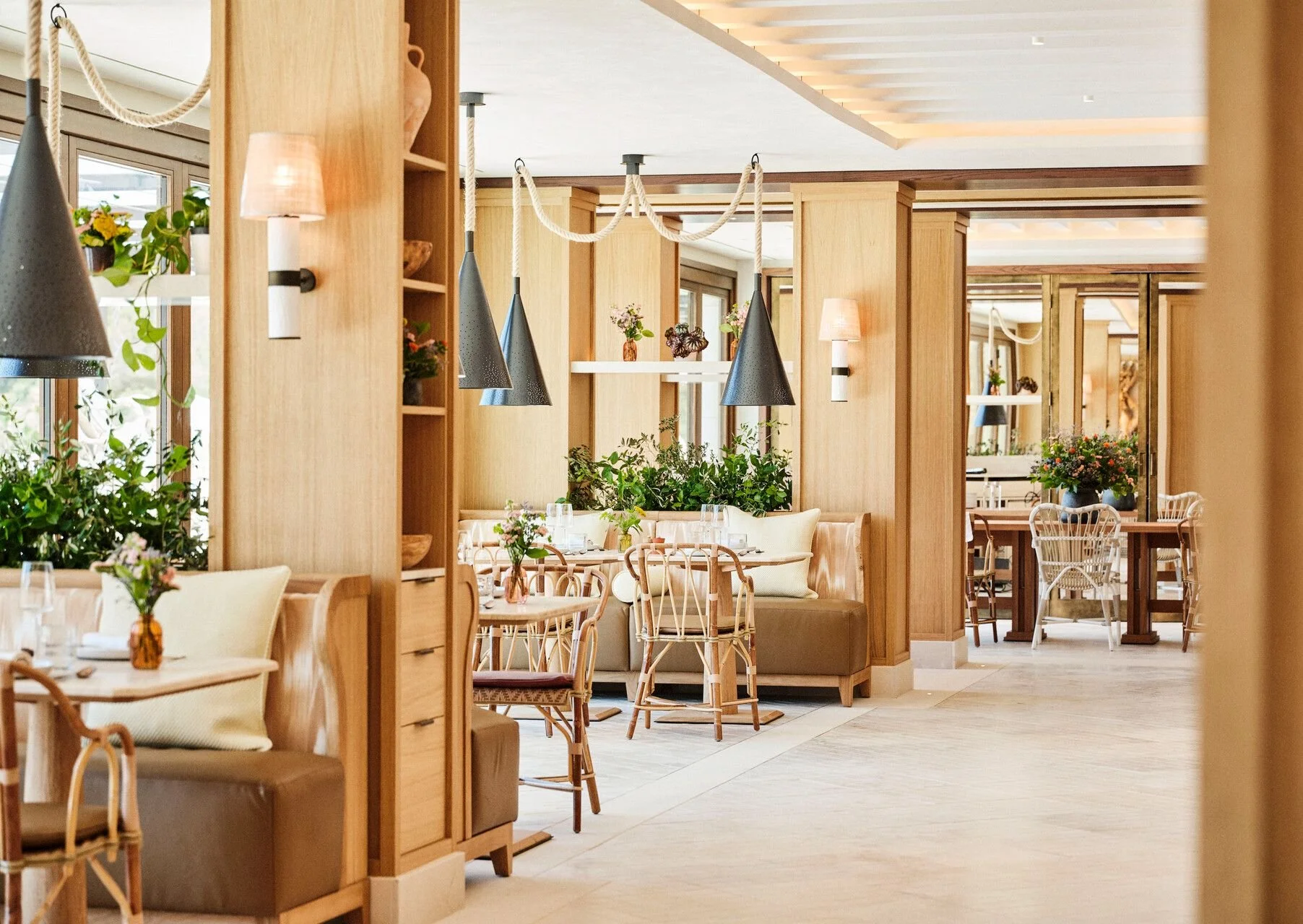 A cozy restaurant interior with wooden partitions, hanging pendant lights, and tables decorated with flowers in brown vases.