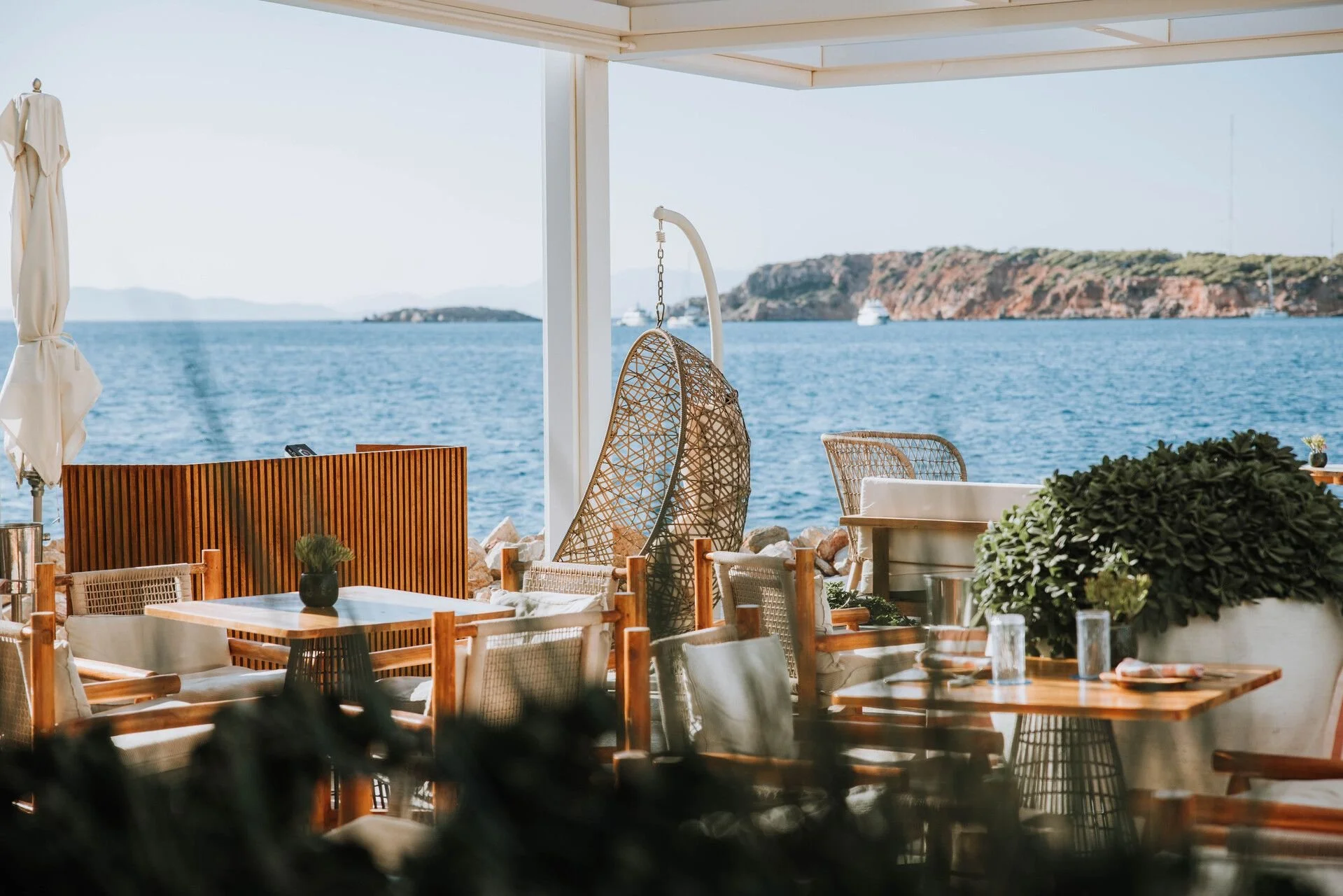 Outdoor restaurant with chairs and tables overlooking a large body of water and rocky cliffs in the background.