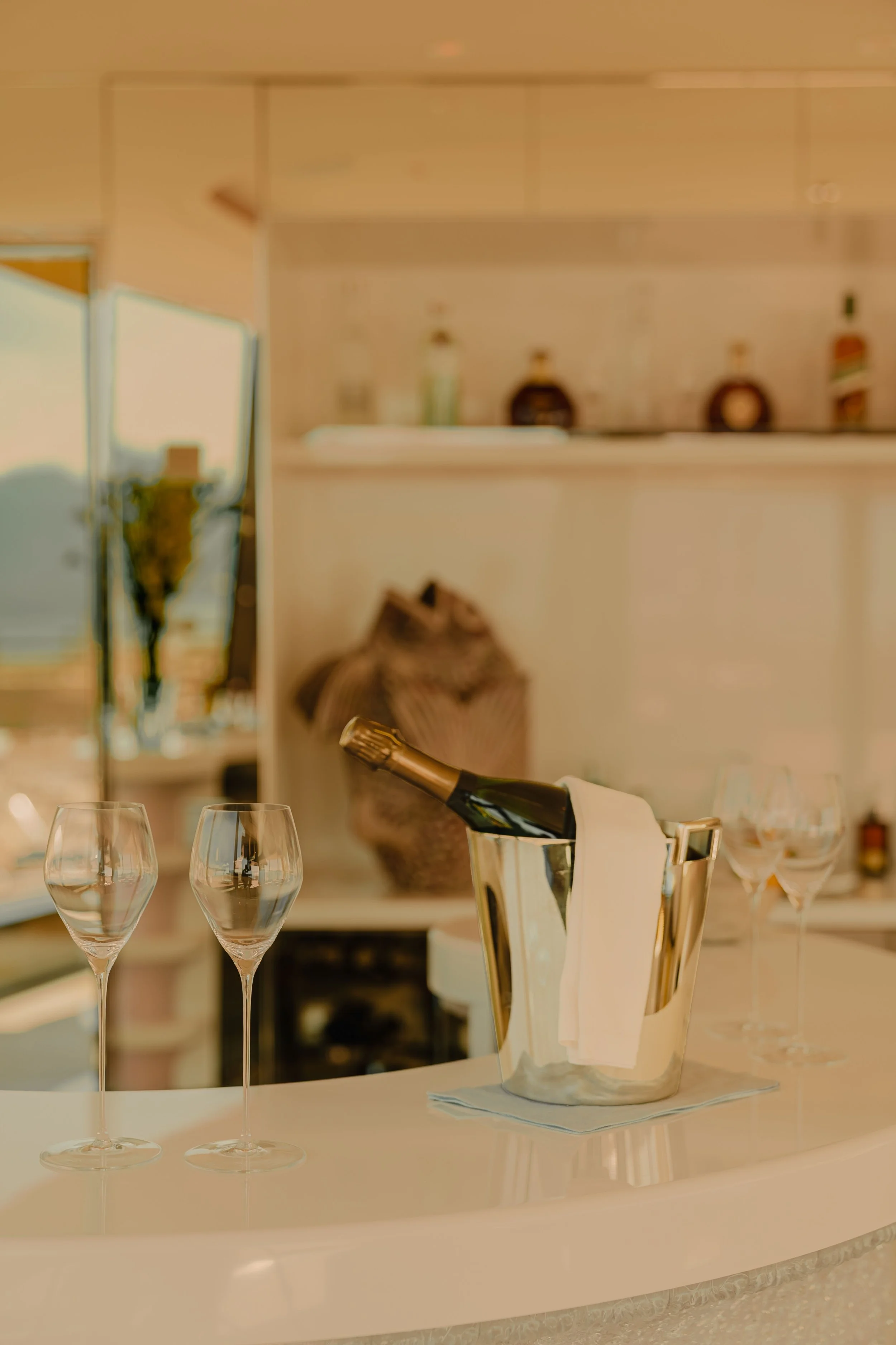 A table with four empty wine glasses, a champagne bottle in an ice bucket with a white napkin, and a folded white napkin.