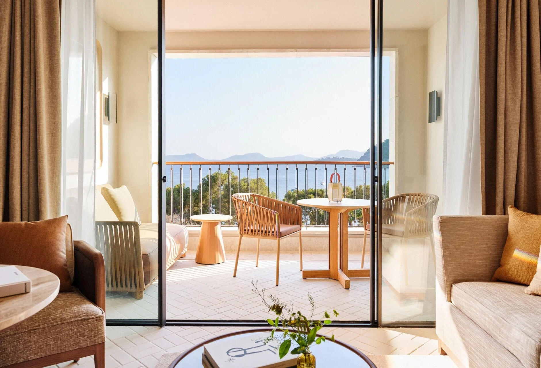 Living room with sliding glass door leading to a balcony with outdoor seating, overlooking mountains and water in the distance.