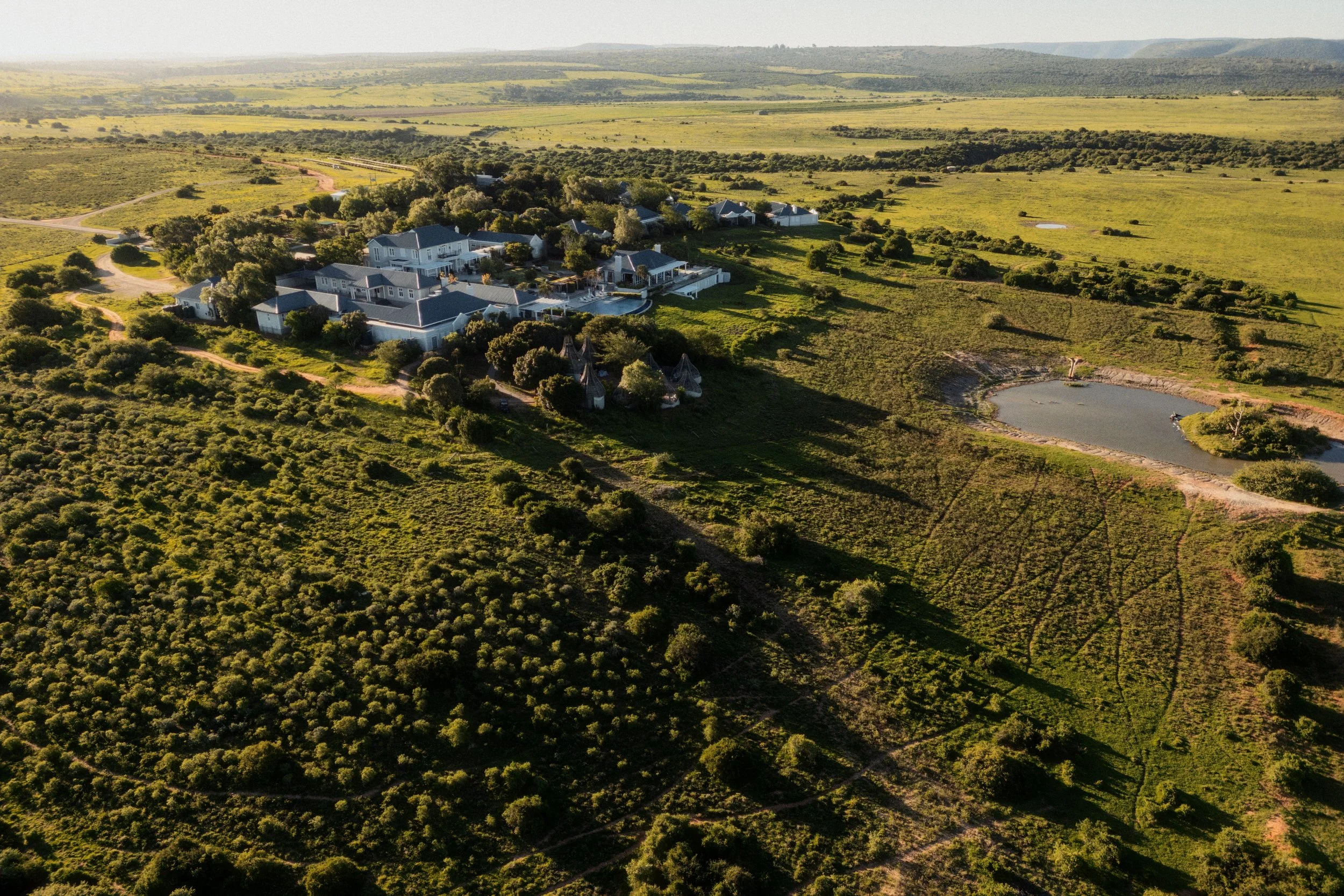 Aerial view of a large residential estate surrounded by green fields and rolling hills, with a small pond and curved driveways.