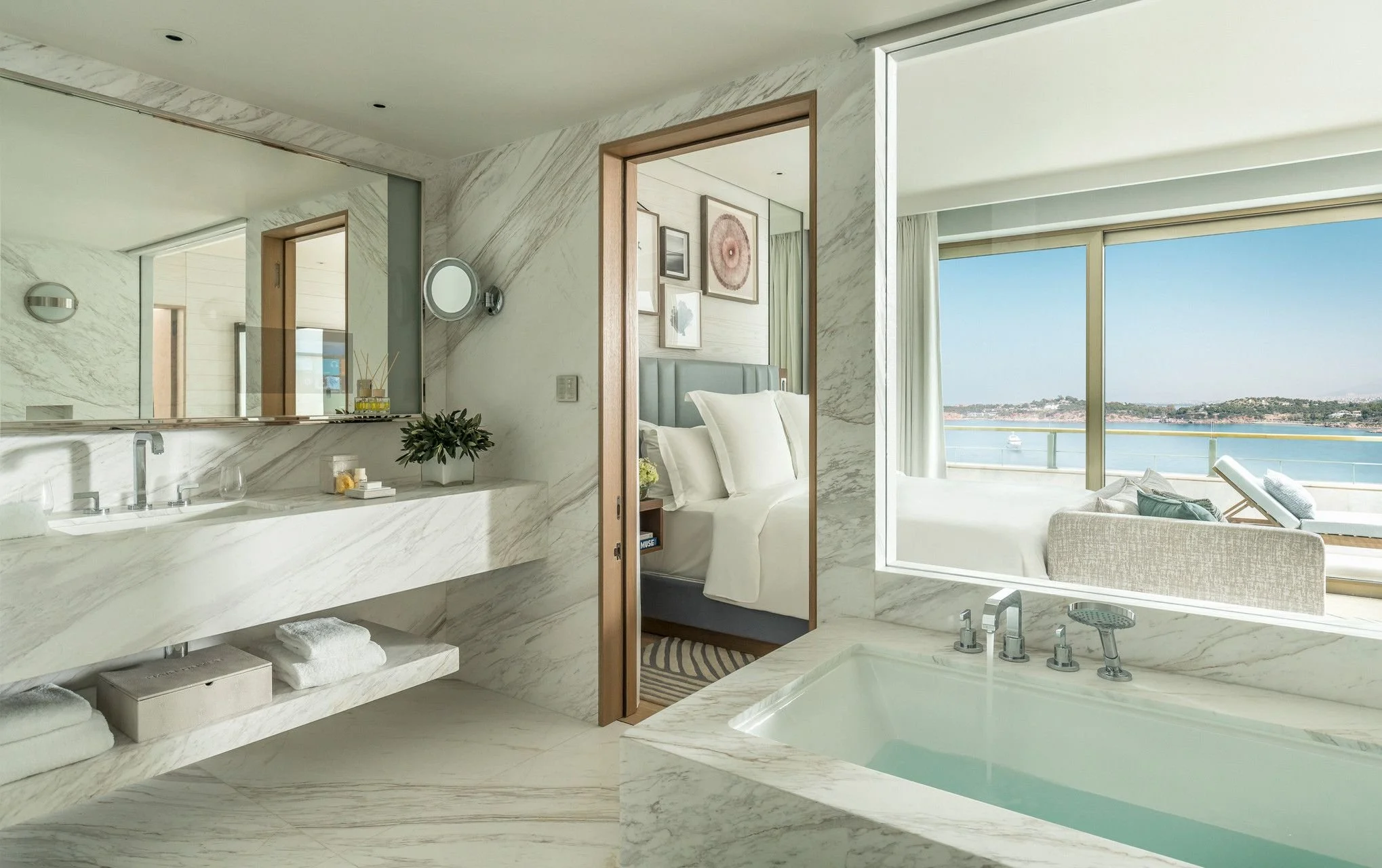 Luxury bathroom with marble surfaces, a soaking tub, and a view of the ocean through large windows.