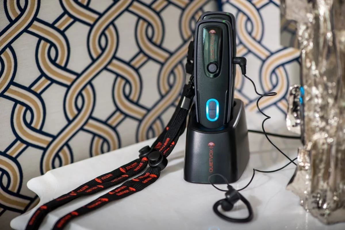 A police body camera mounted on a charging dock, with a lanyard attached, placed on a white surface. A decorative background is visible behind the camera.