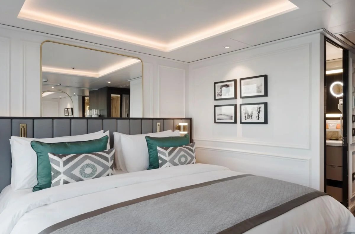 A modern hotel room with a large bed, decorative pillows, a mirror, wall art, and a glimpse of a bathroom.