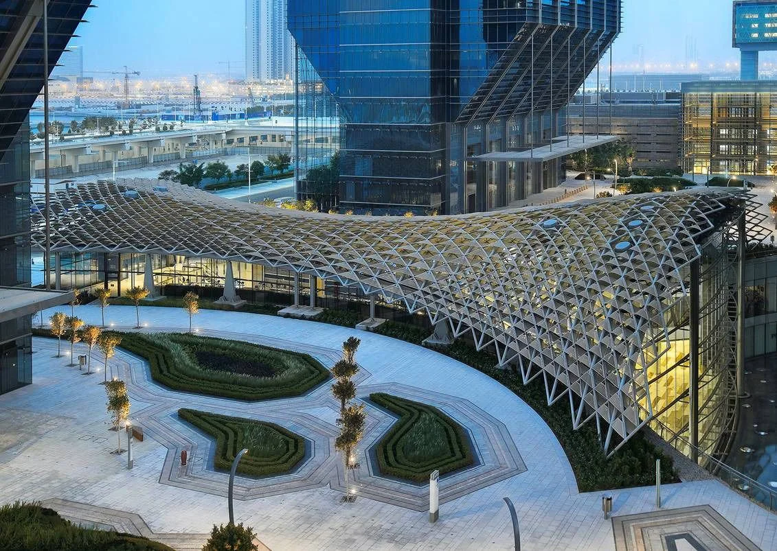 Modern glass building with a curved lattice canopy and landscaped pathway