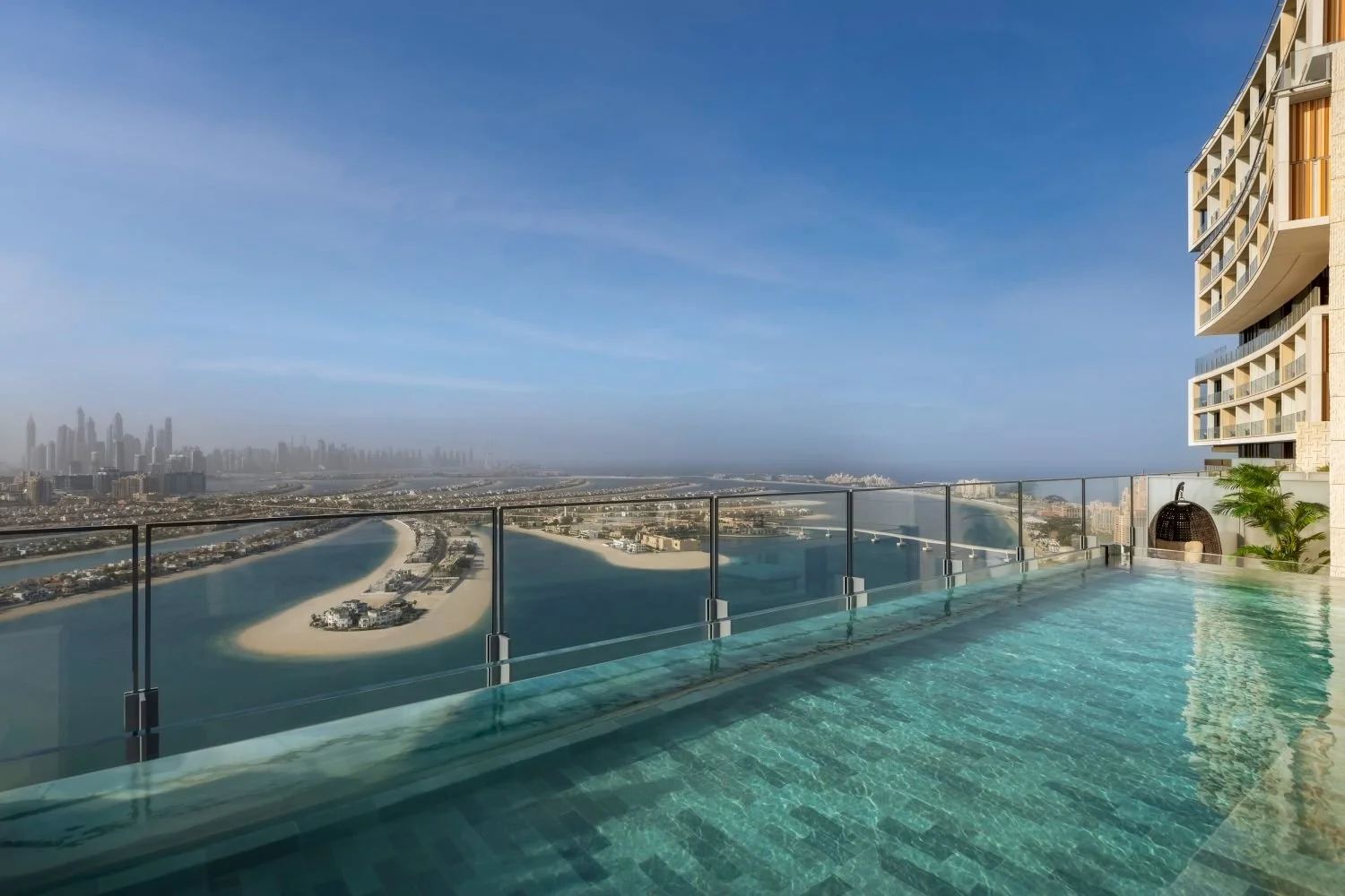 Infinity pool on a high-rise building with a glass railing, overlooking a cityscape and waterway with a distant skyline of tall buildings.