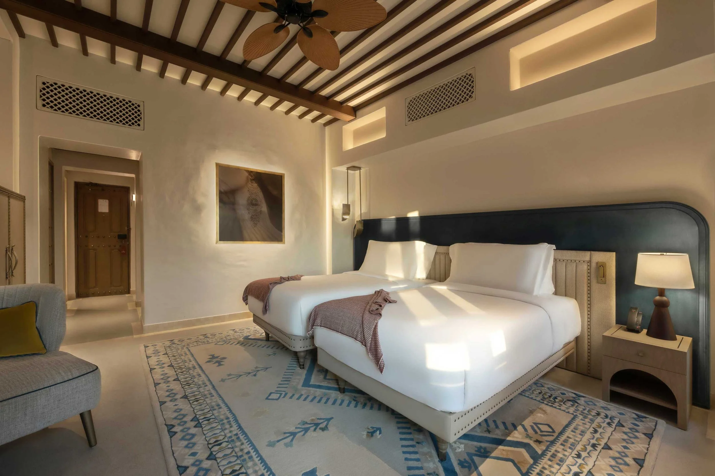 A bedroom with a white bed, wooden nightstand, reading lamps, framed artwork, and a ceiling fan in the ceiling.