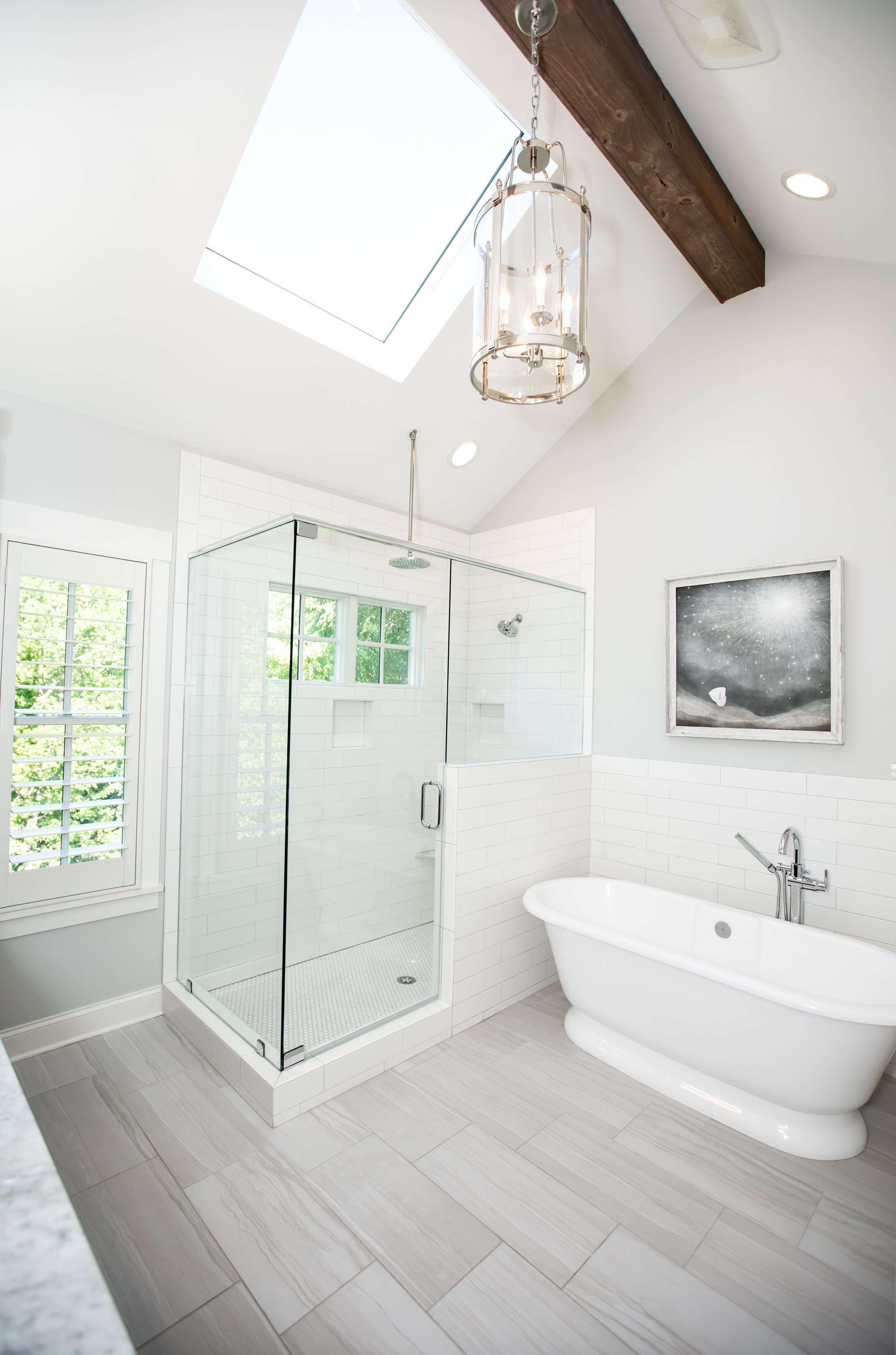 Modern bathroom with a skylight, a glass-enclosed shower, a freestanding bathtub, a framed artwork, and light-colored wooden flooring.