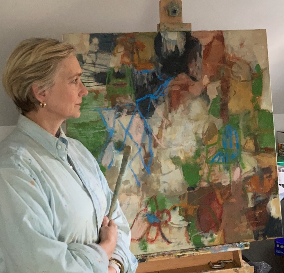 Woman standing next to an abstract painting on an easel, wearing a white smock and holding a paintbrush.