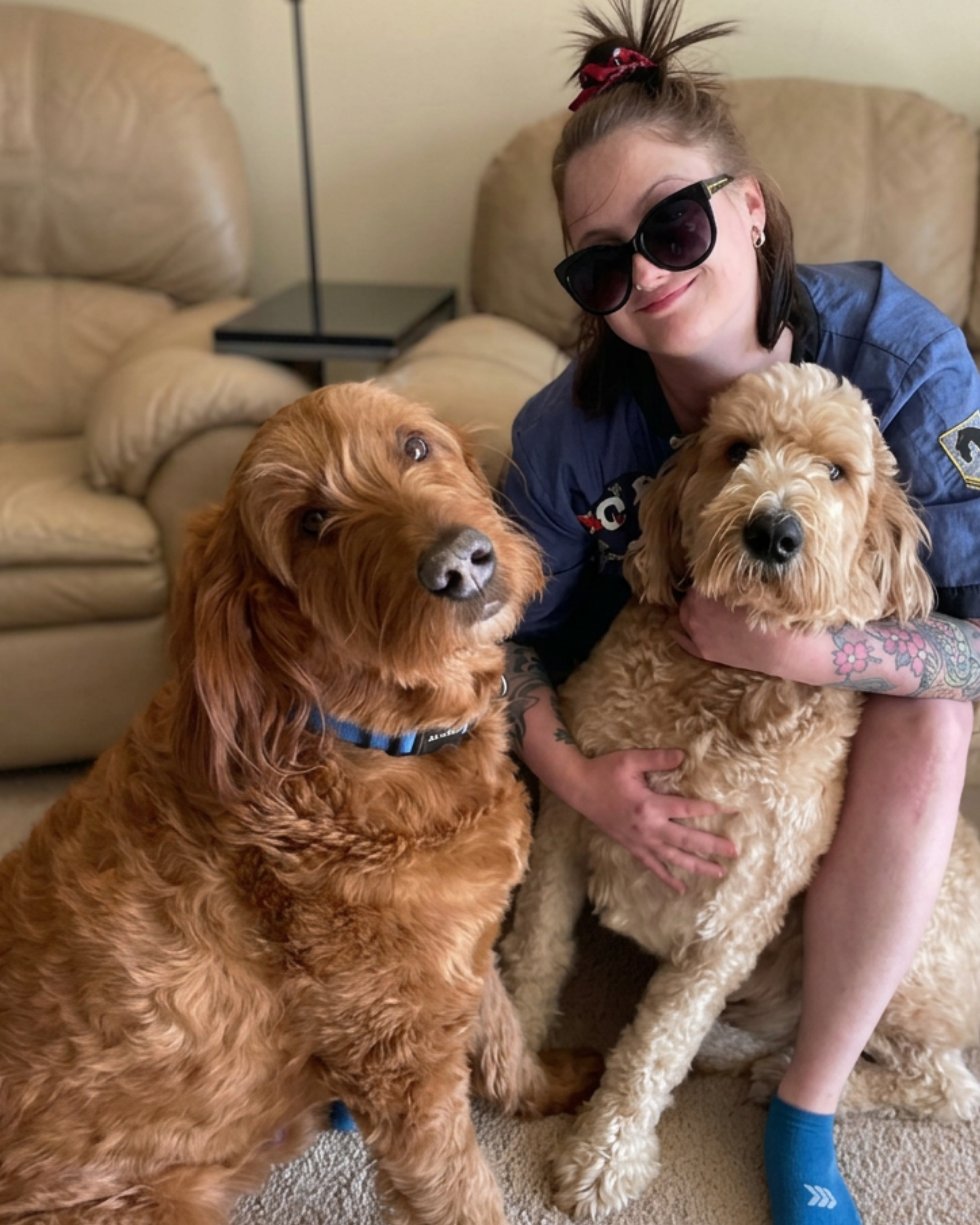 Smiling with two dogs, one large golden retriever and one smaller curly-haired dog.