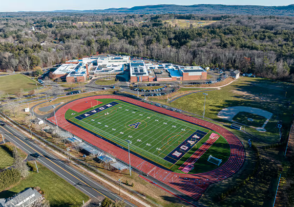 An aerial view of a high school campus with a football field and surrounding track, and a school building in the background.