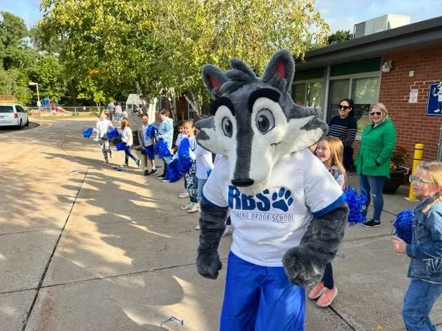 A person dressed as a wolf mascot in a white and blue shirt with 