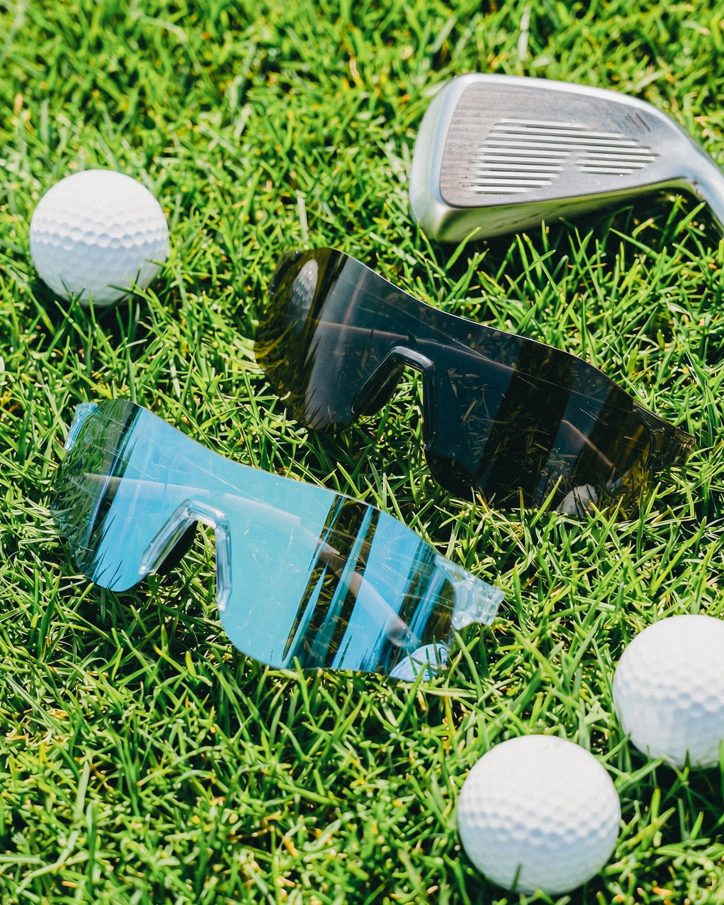 Golf ball and golf club on grass with sunglasses nearby.