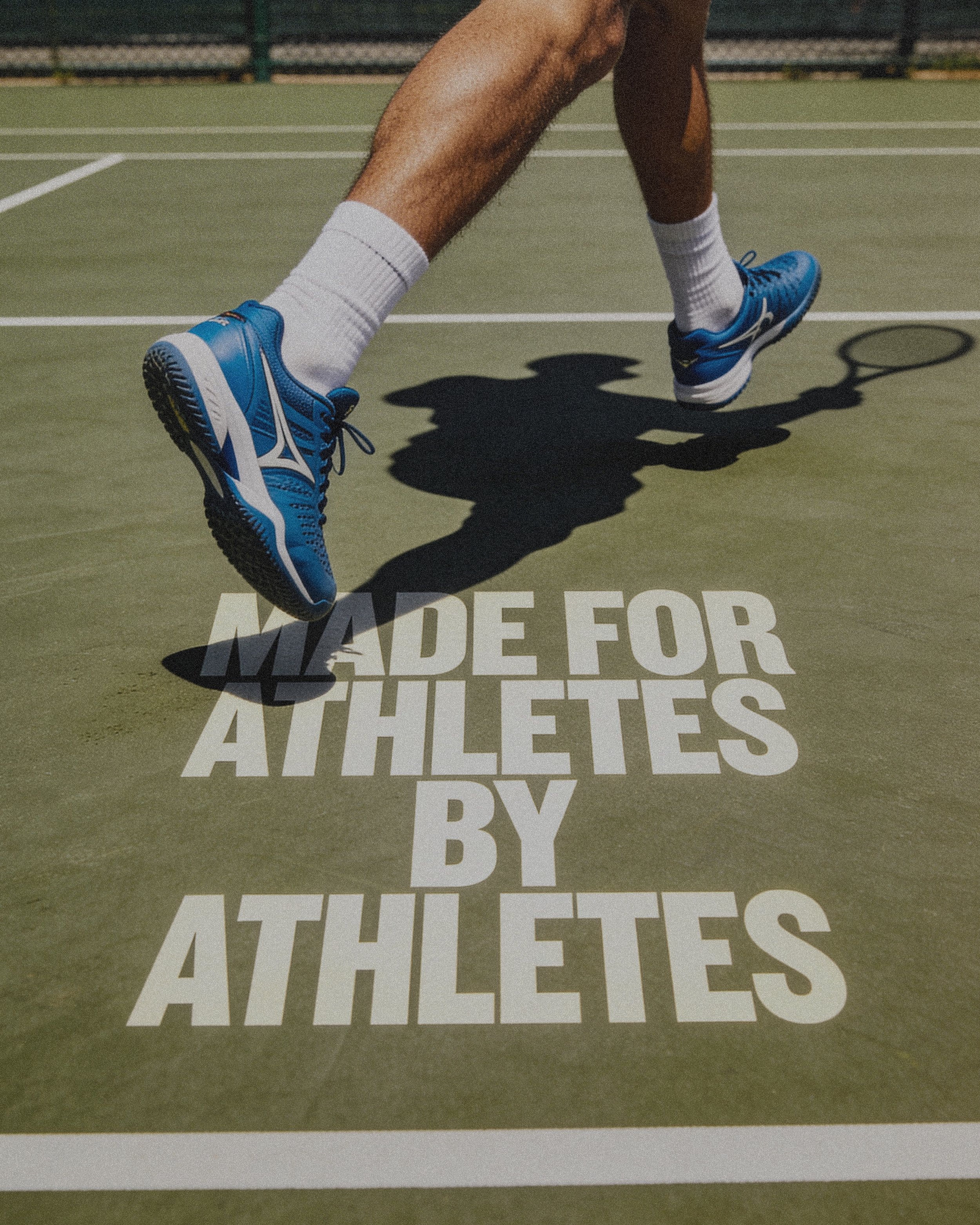Close-up of a tennis player in a ready position on a tennis court, showing their legs, tennis shoes, and shadow on the court with a motivational message printed on the court surface.