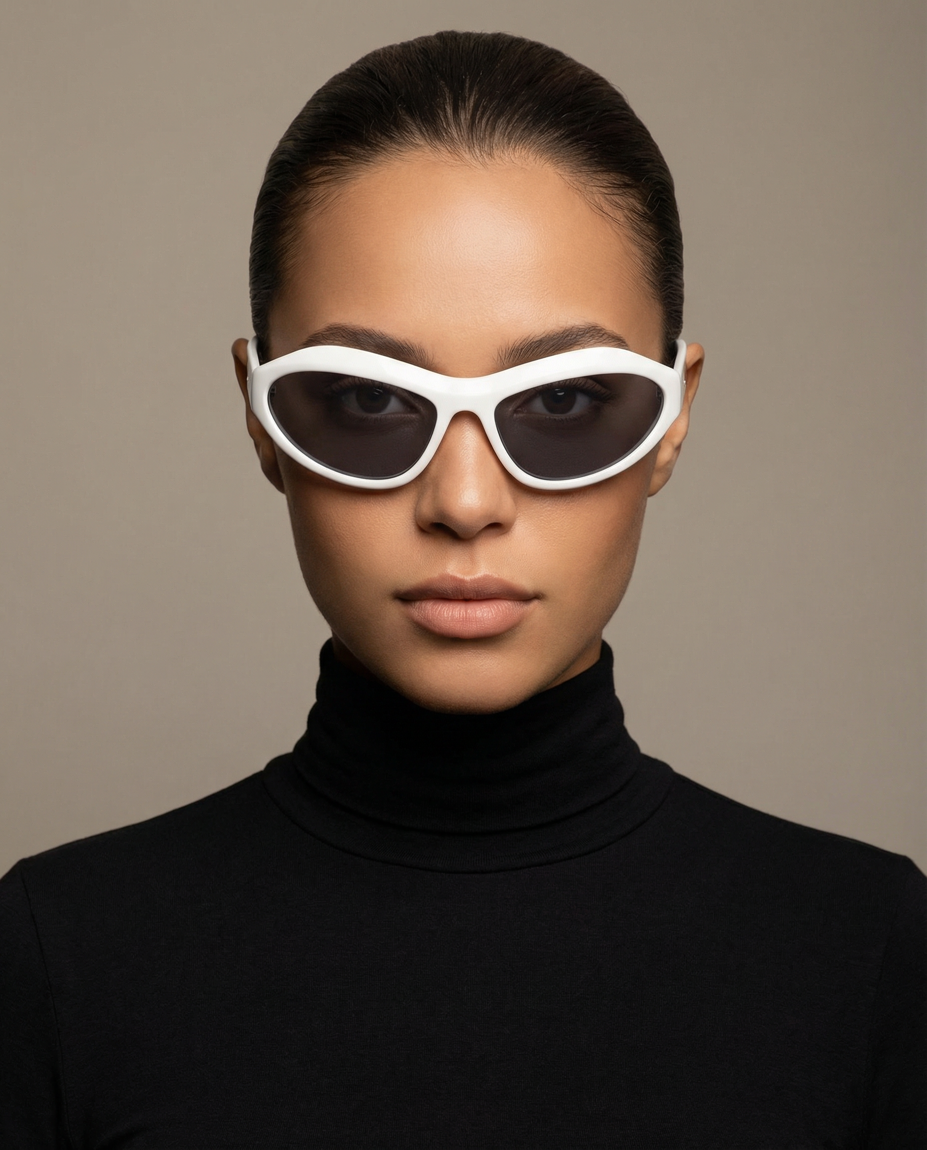 A woman with dark hair pulled back is wearing large white sunglasses with dark lenses and a black turtleneck, standing against a neutral background.
