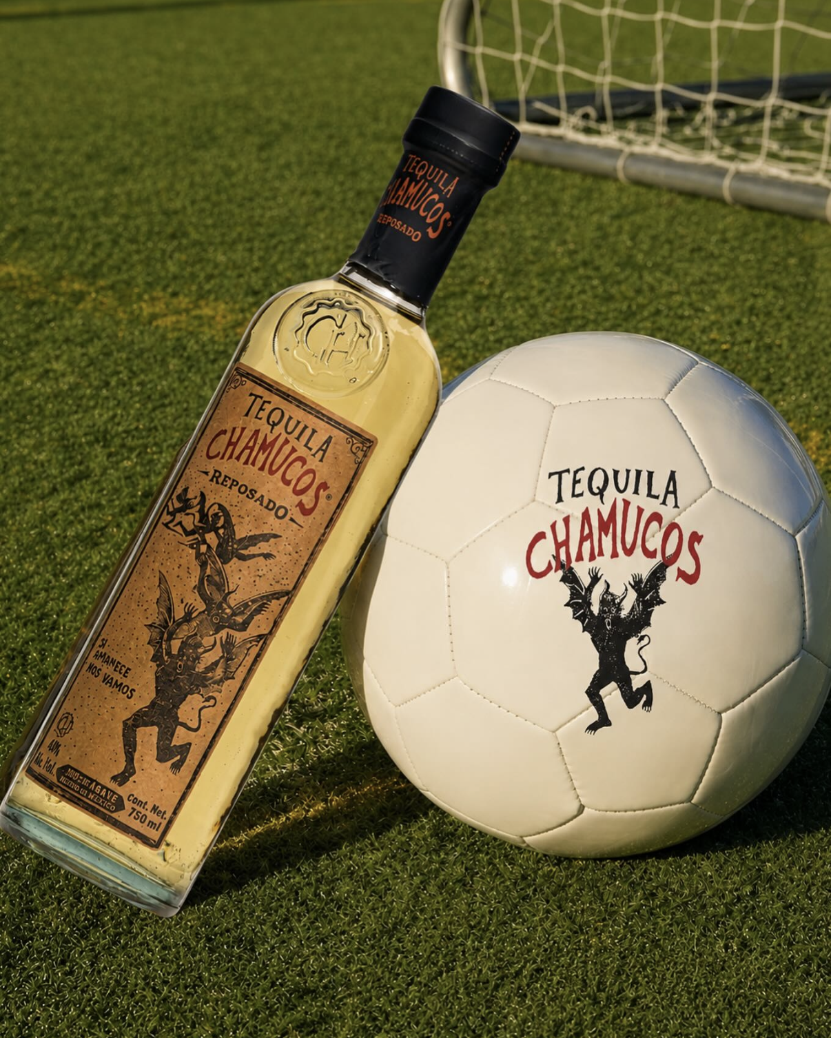 A bottle of Chamucos Reposado tequila leaning against a football with the Chamucos logo on it, on a football field.