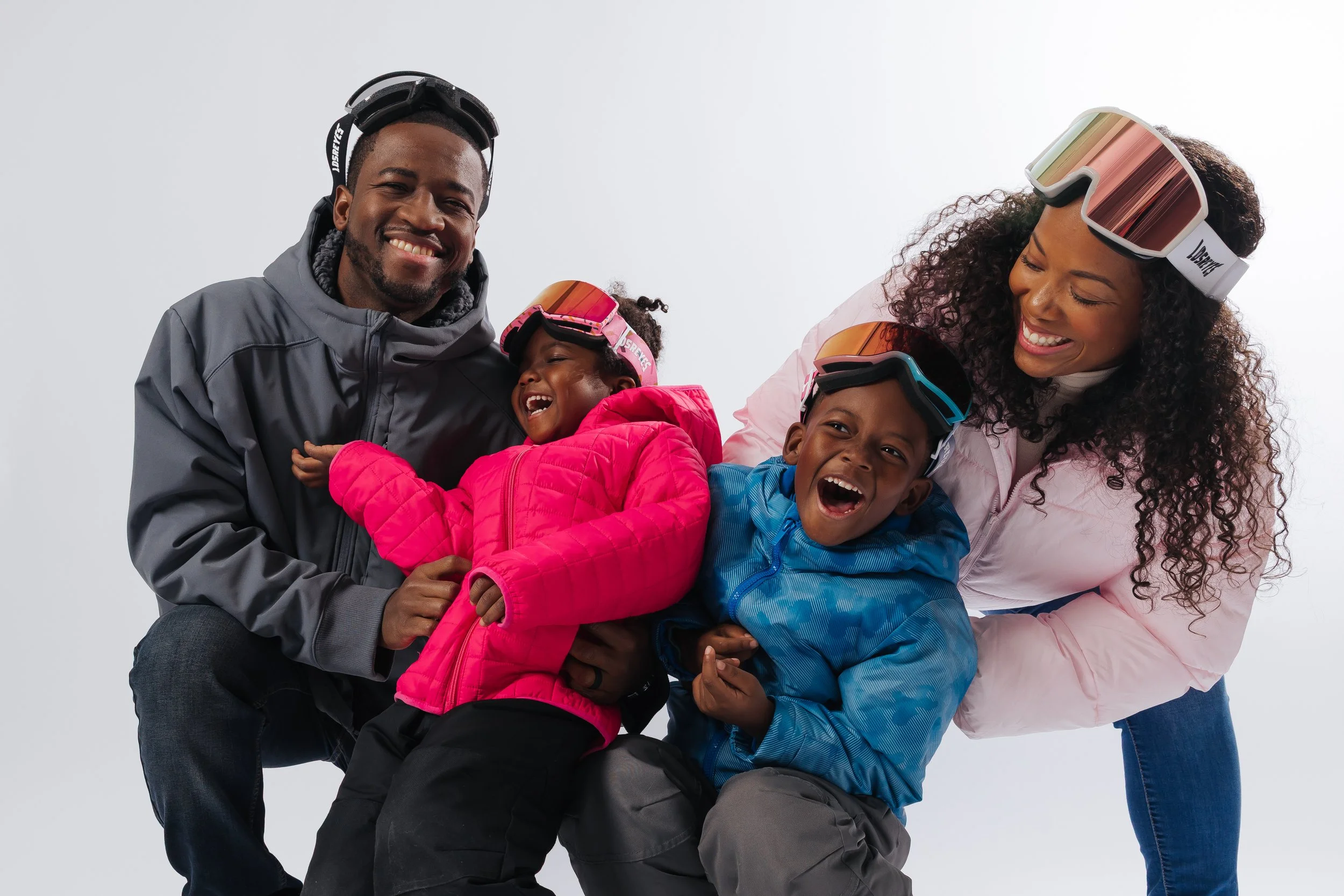 A happy family of four, outdoors in winter gear, laughing and embracing each other, with white background.