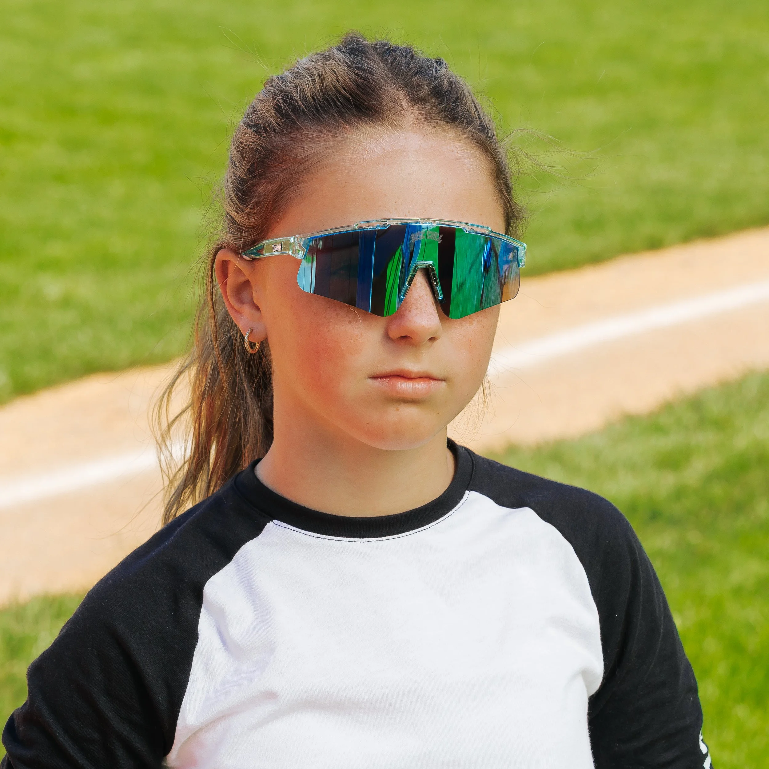 Close-up of a woman wearing sports sunglasses outdoors, with greenery in the background.