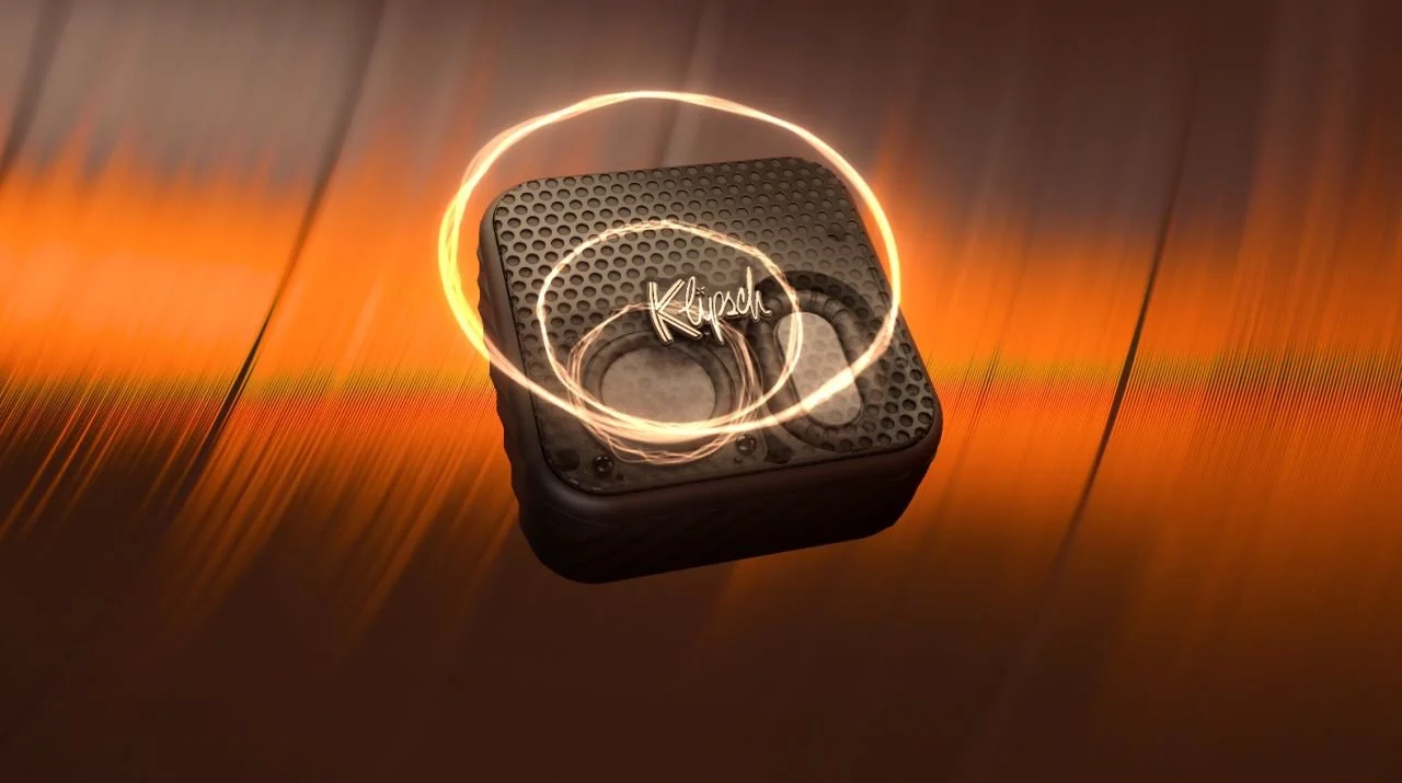 A Black Klipsch portable speaker with a textured surface, surrounded by swirling light effects, on a wooden surface with warm lighting.