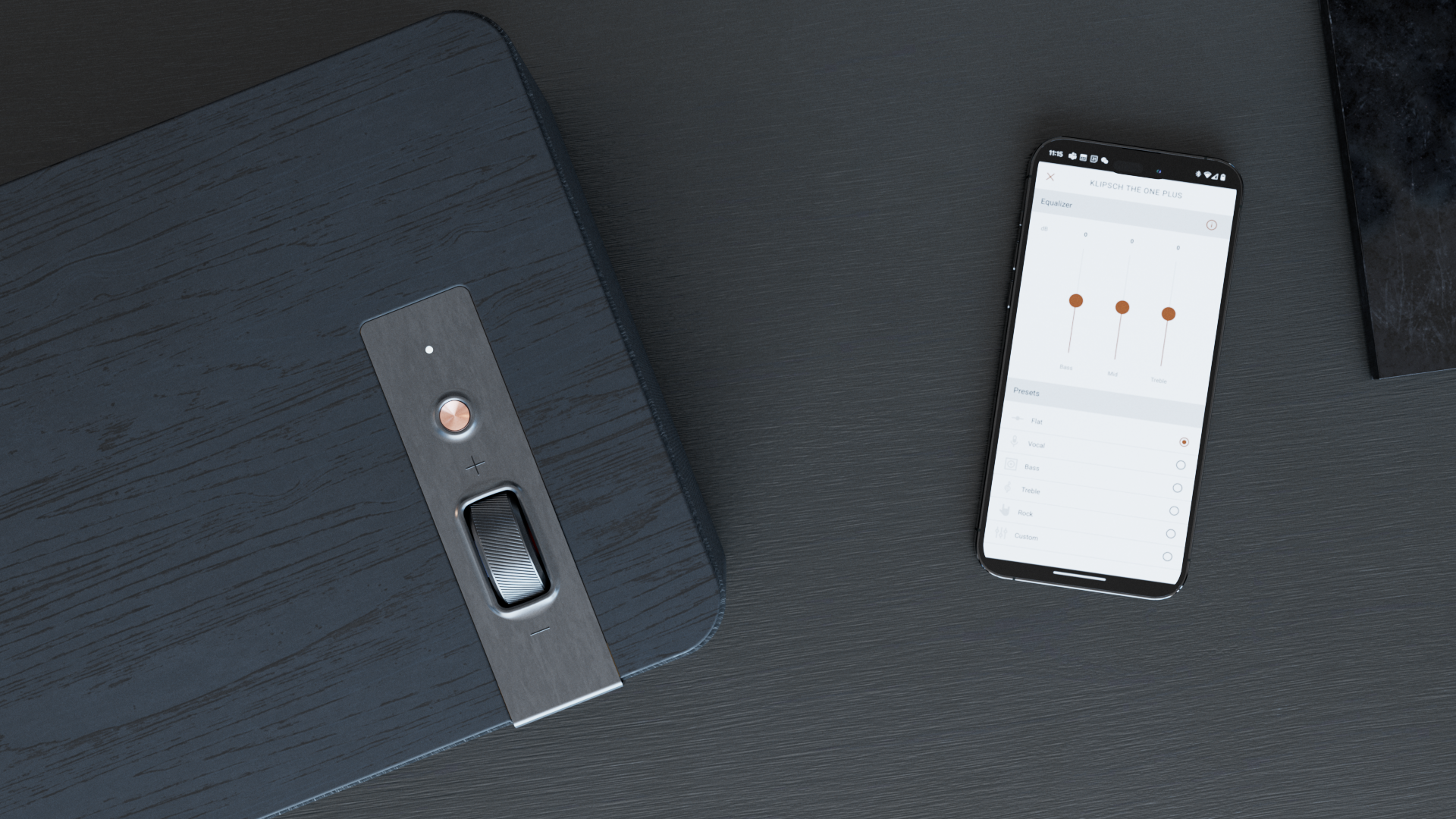 A black wooden speaker with a silver control panel and a smartphone displaying an equalizer app on a black wooden surface.