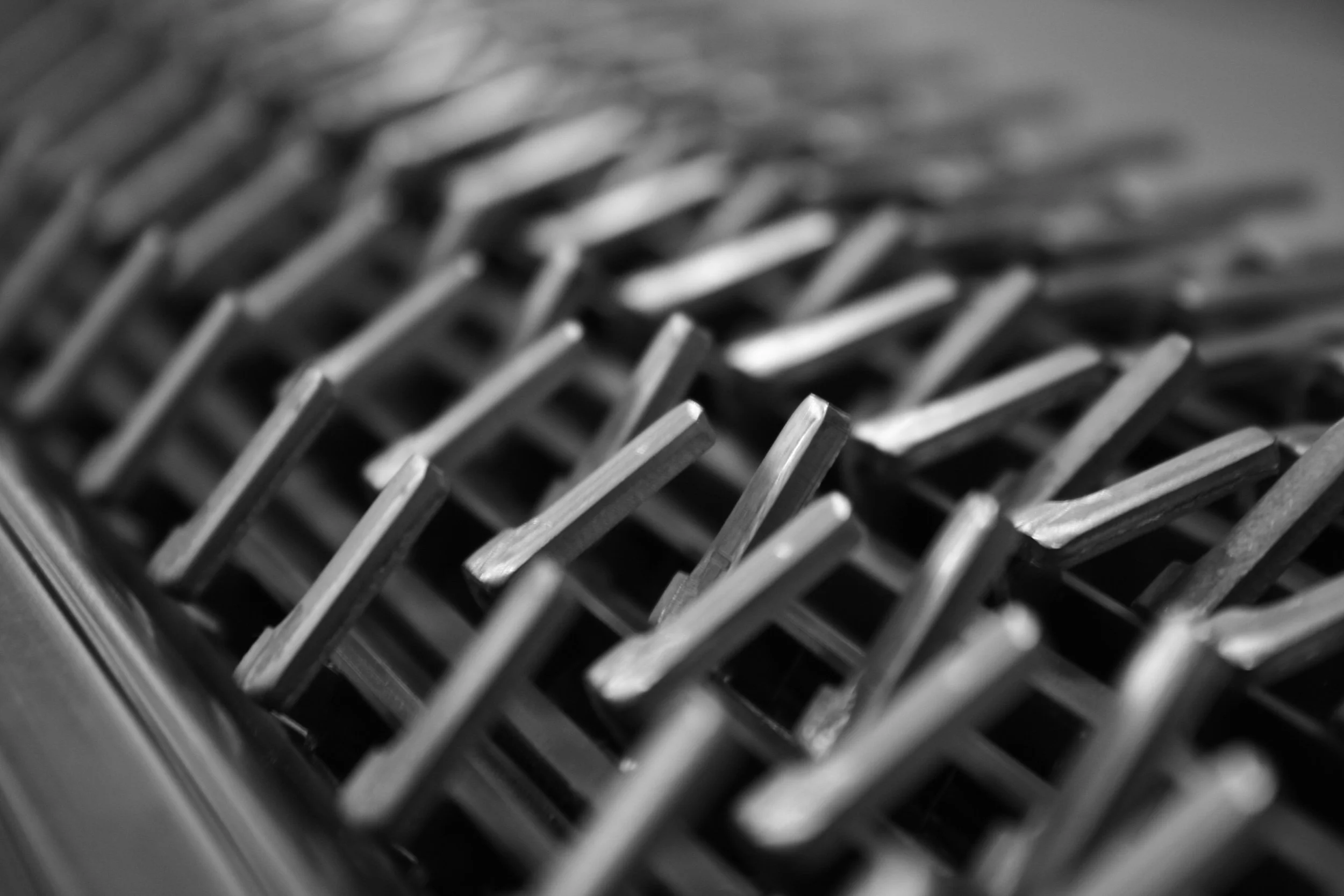 A close-up black-and-white photograph of a metal grate or vent with intersecting bars creating a grid pattern.