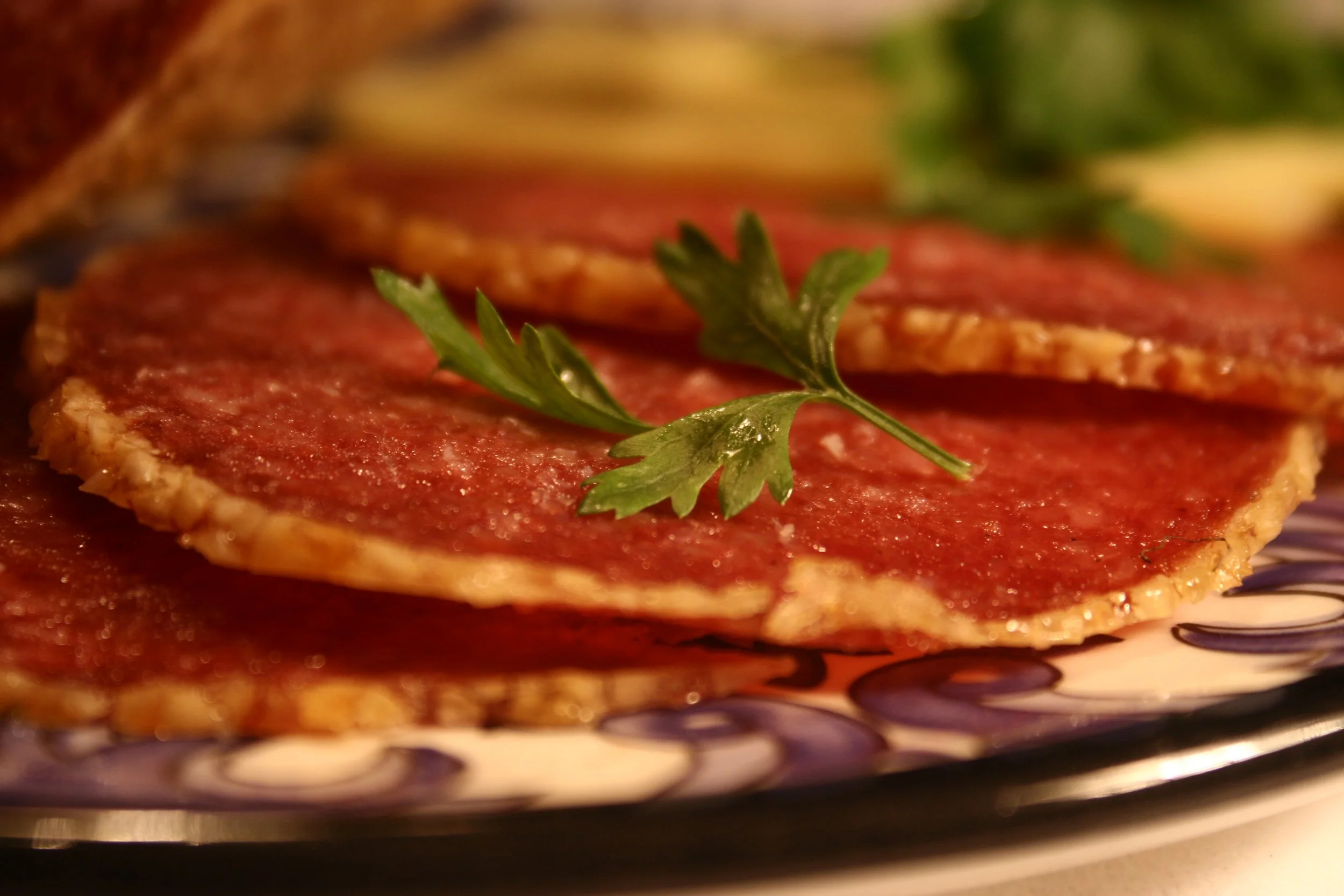 Close-up of raw ground beef patties topped with a sprig of parsley, on a decorative plate.