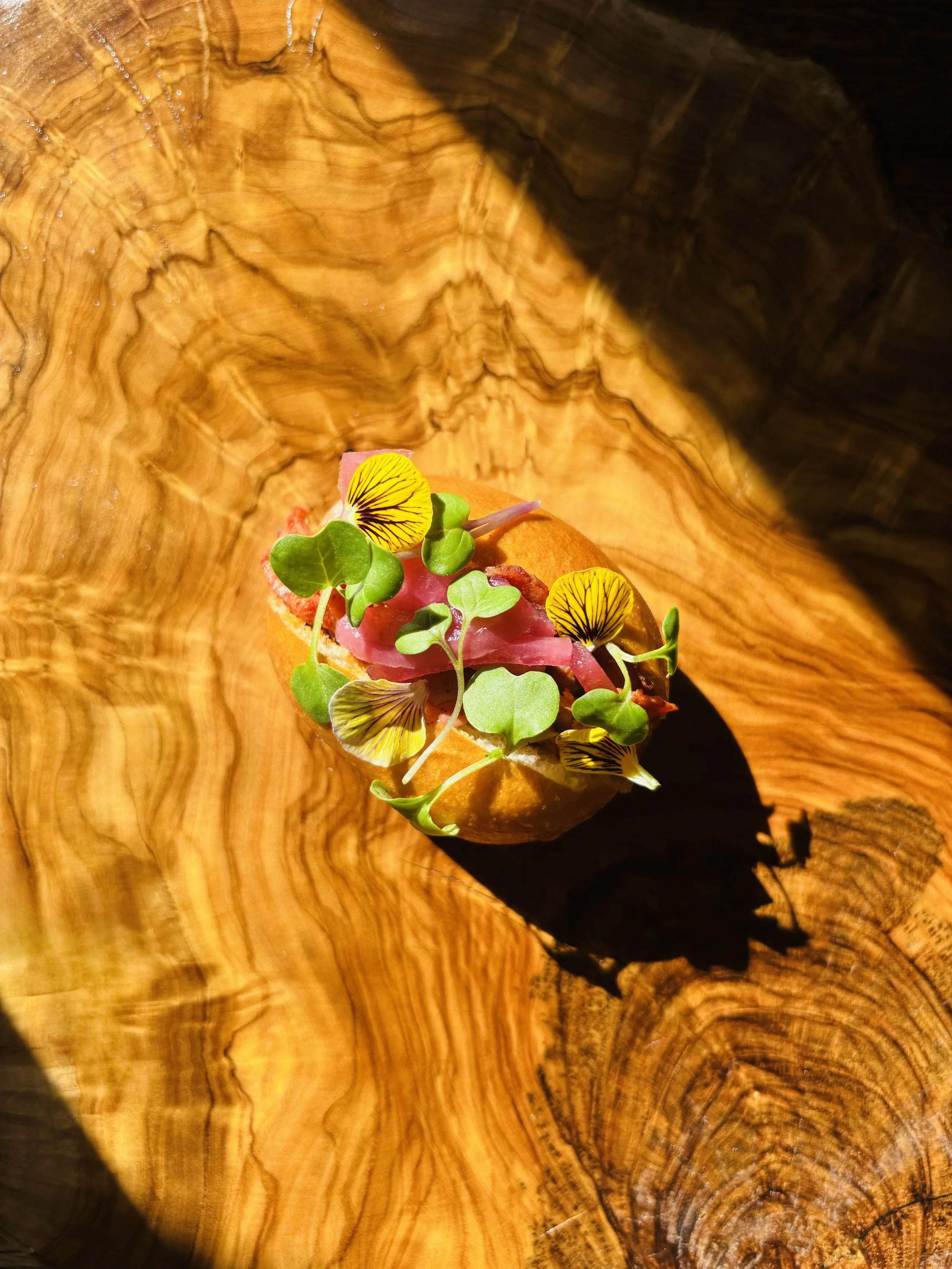 Un plat présenté sur une planche en bois avec des éléments végétaux et fleurs decoratives