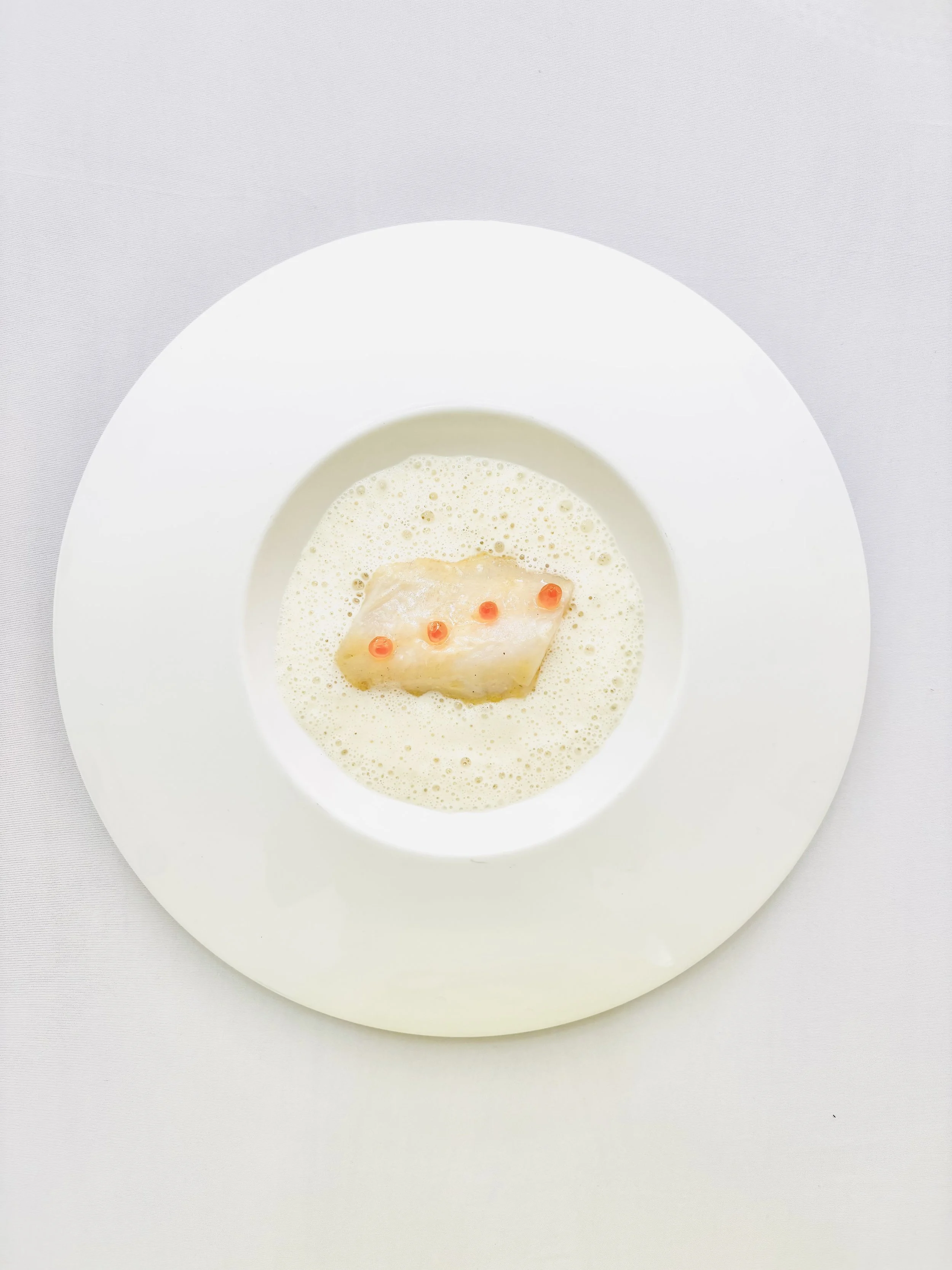 Poisson dans une sauce crémeuse, garniture de petites gouttes oranges, présenté dans une assiette blanche.