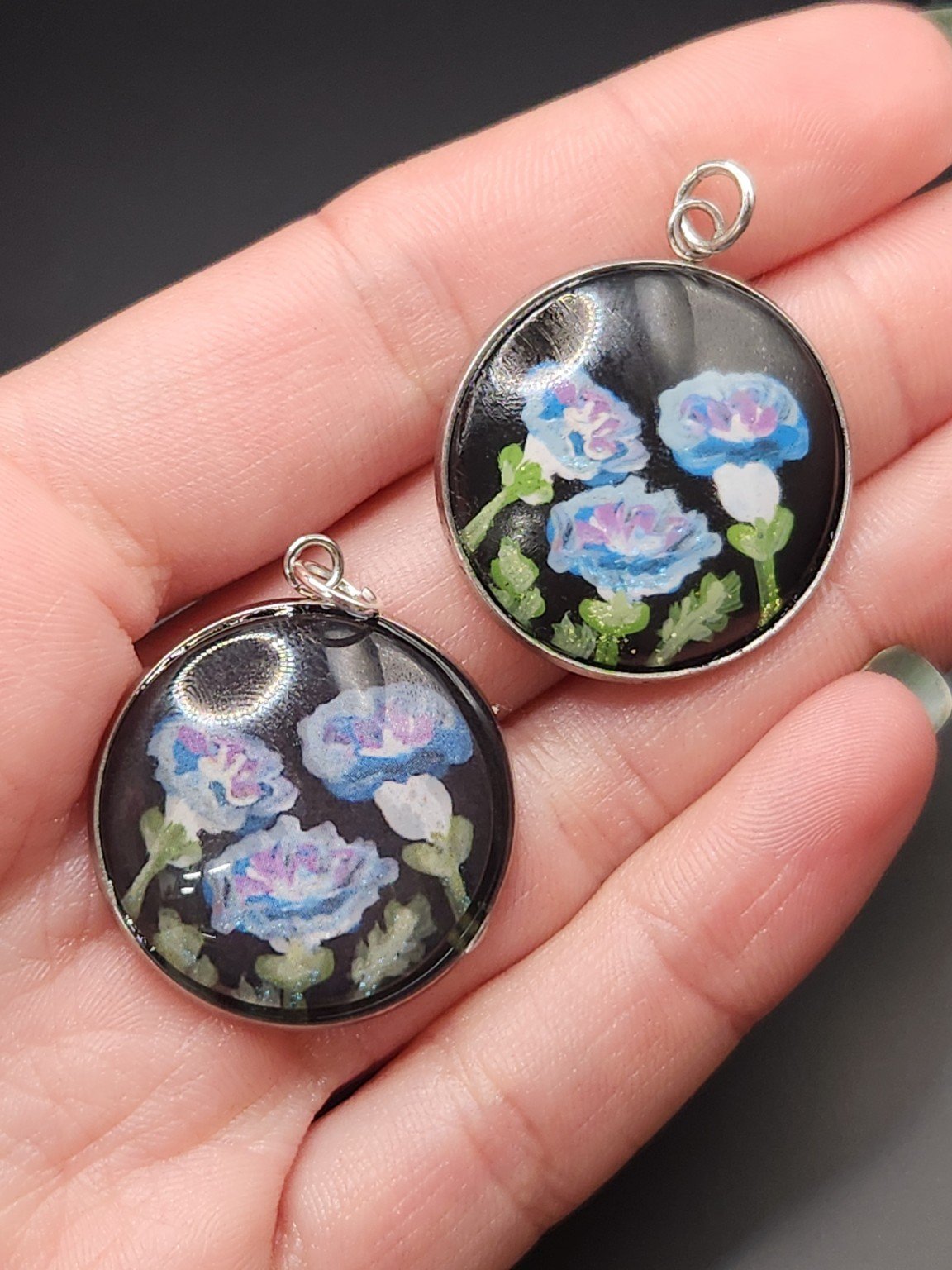 Two morning glory pendants held in a hand: hand-painted original at the top right and printed reproduction at the bottom left.
