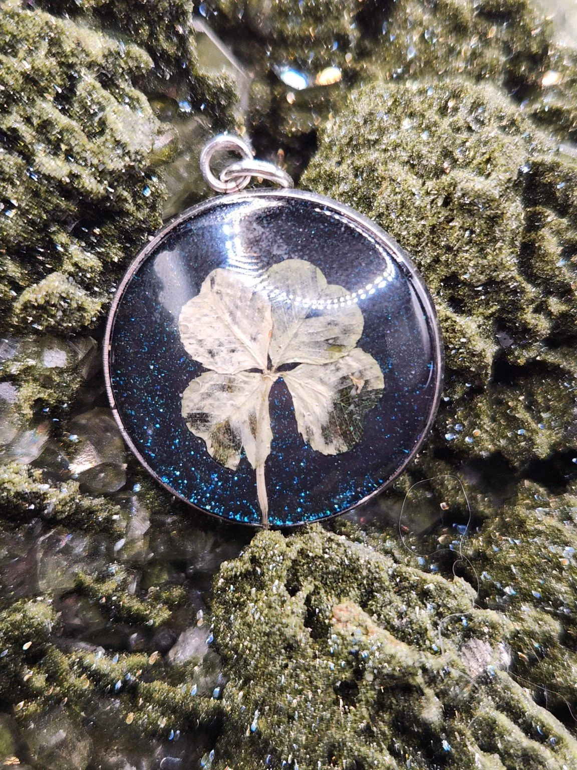 Naturally Unique N004: real four-leaf clover pendant with blue glitter on a crystal display. Display not included.