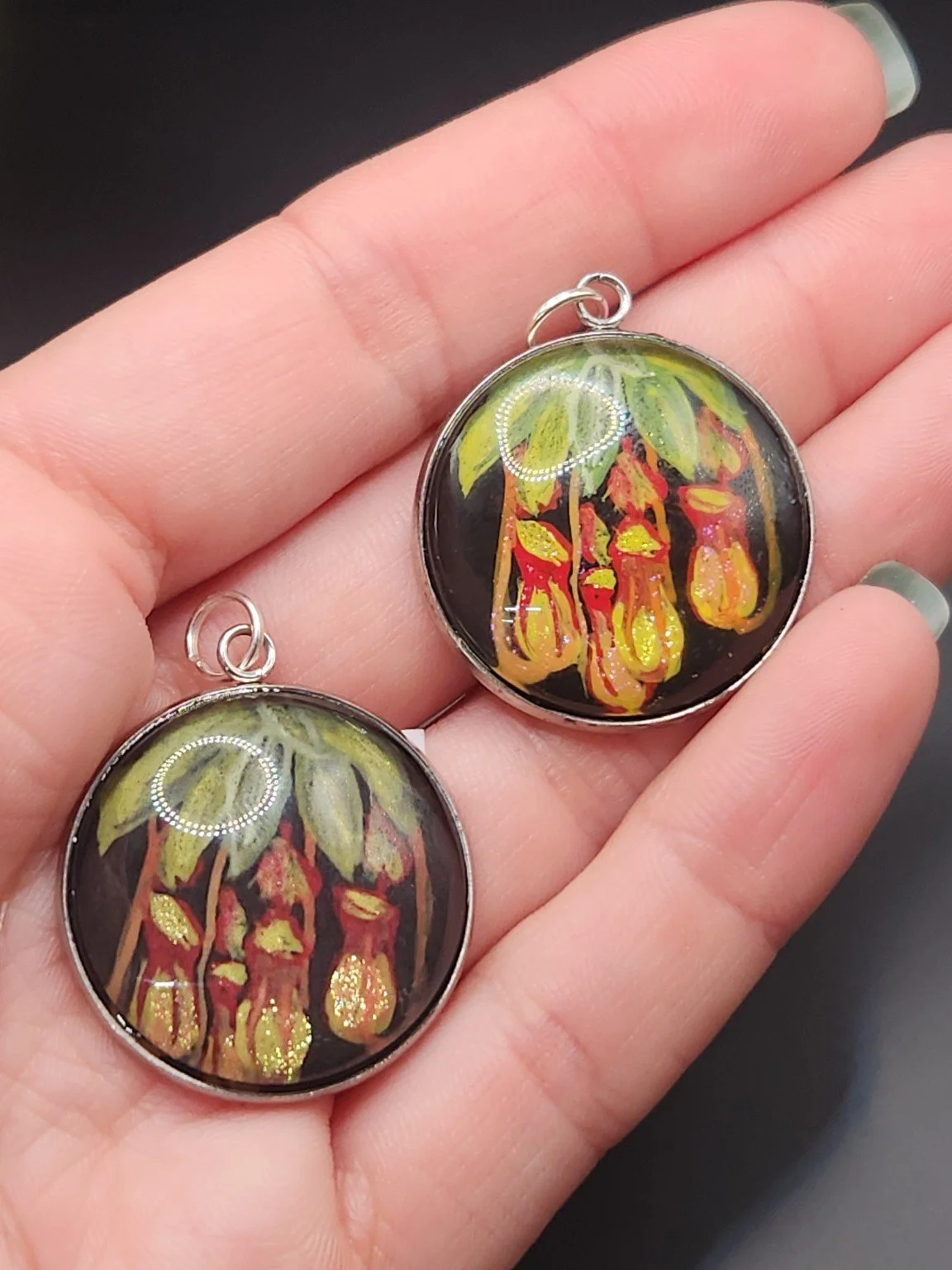 Pitcher plant pendant comparison held in a hand: the hand-painted original is at the top right, and the printed reproduction is at the bottom left.