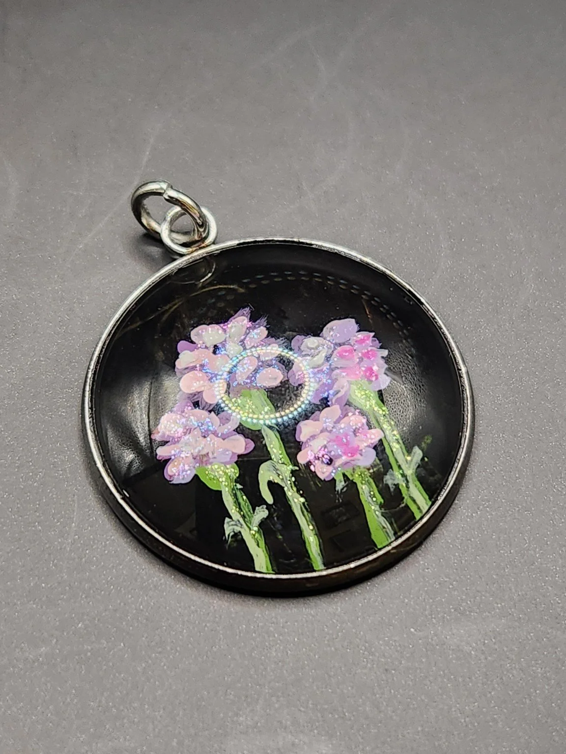 Pink and purple carnation flower art pendant with green stems and shimmering glitter accents on a gray background.