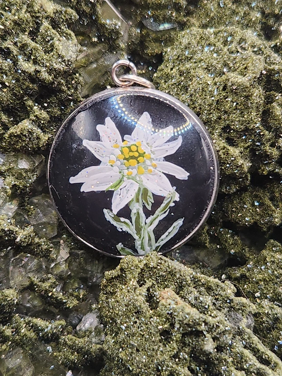 White edelweiss flower art pendant resting on a green crystal display. Crystal display not included.