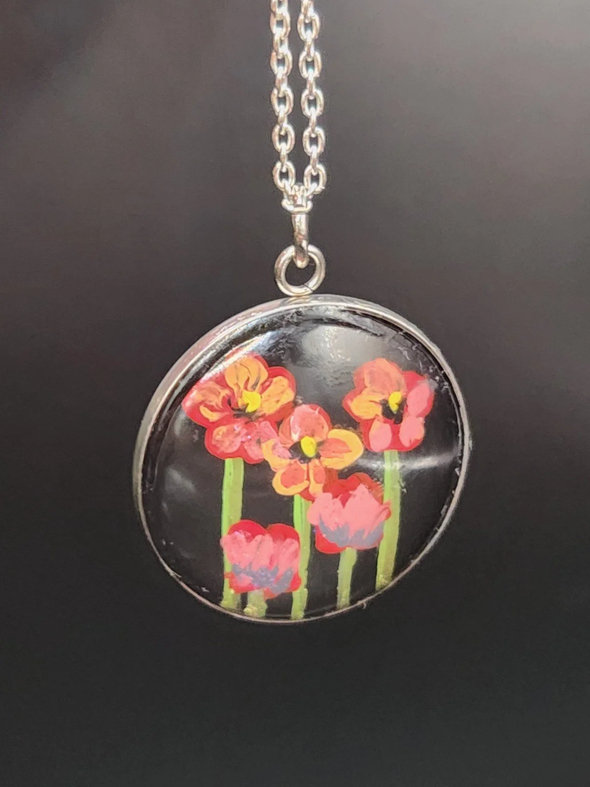 Red and pink poppy flower art pendant hanging from a silver-tone chain against a dark background. Chain not included.