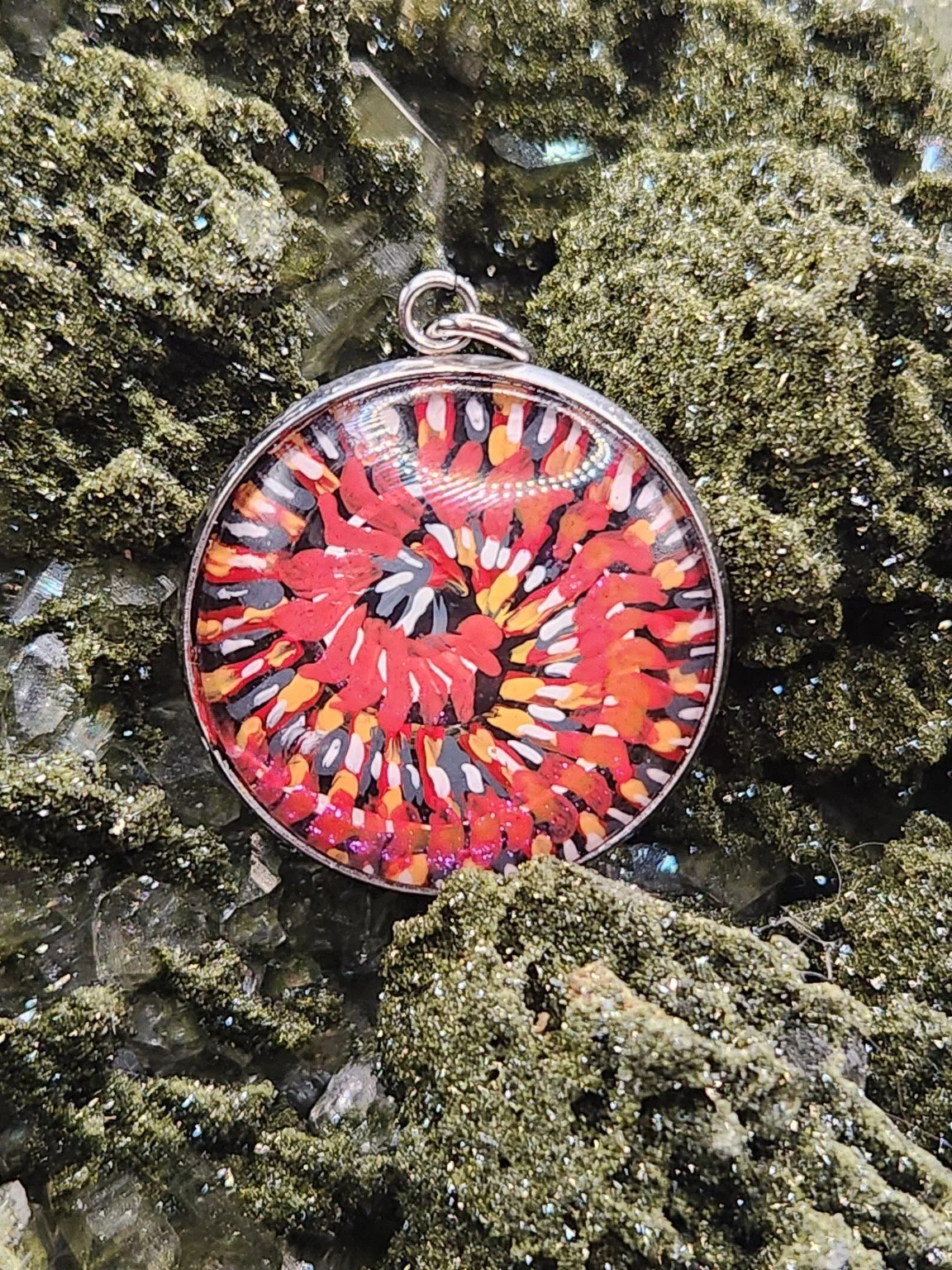 Coiled red-and-orange Millipede Design 1 art pendant resting on a green crystal display. Crystal display not included.