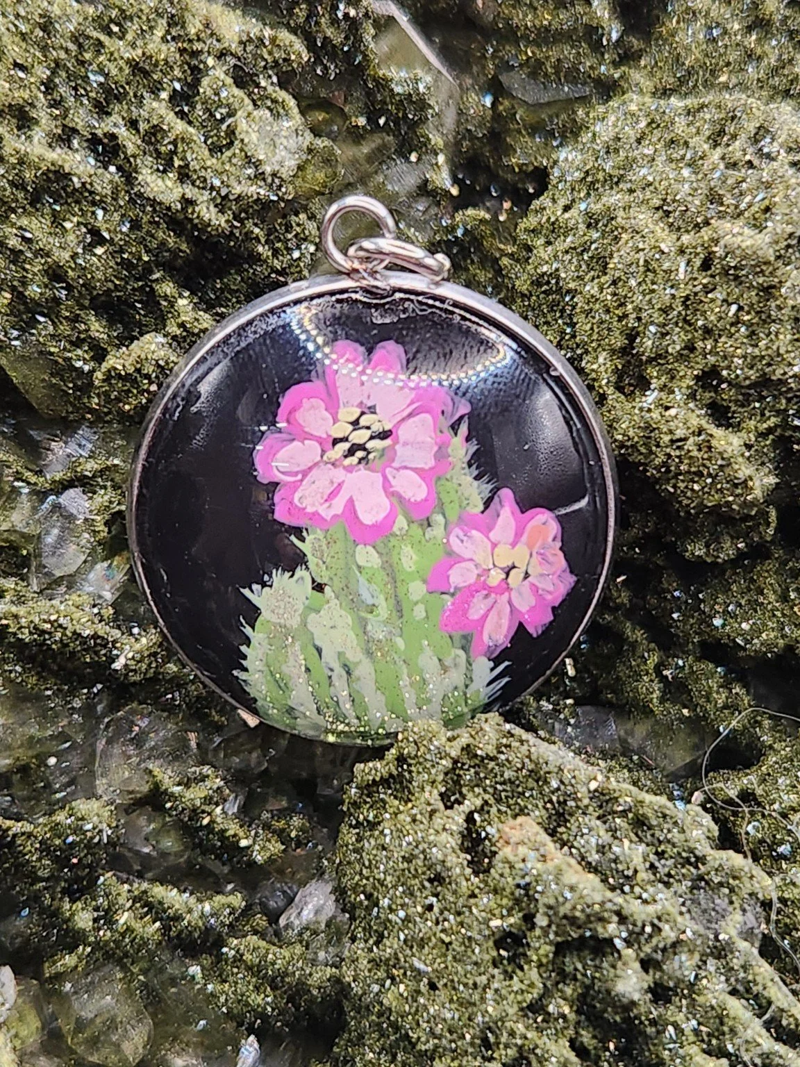 Cactus flower art pendant displayed among green crystals. Crystal display and styling props not included.