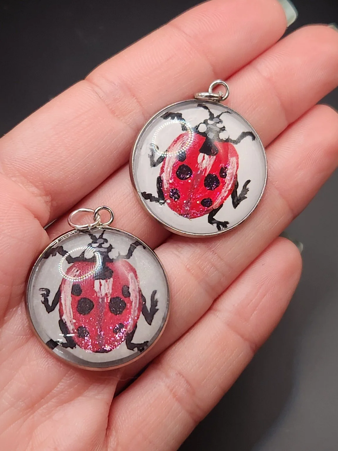 Ladybug pendant comparison held in a hand: the hand-painted original is at the top right, and the printed reproduction is at the bottom left.