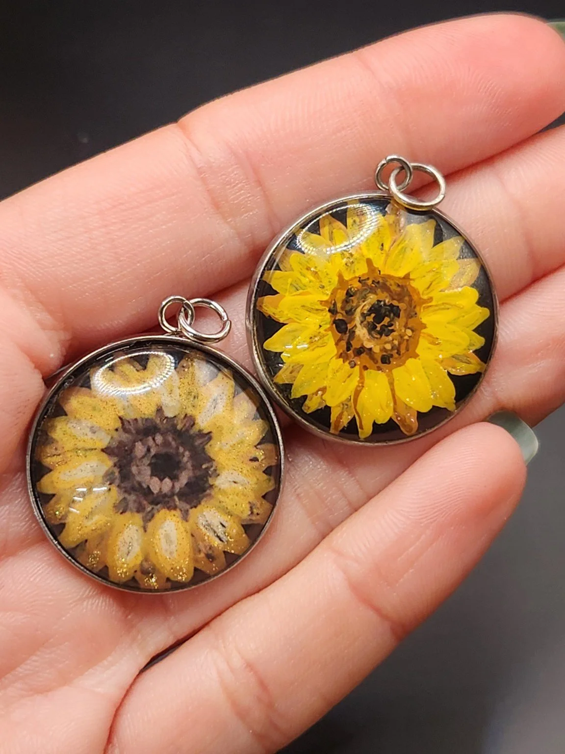 Two sunflower pendants held in a hand: hand-painted original at the top right and printed reproduction at the bottom left.