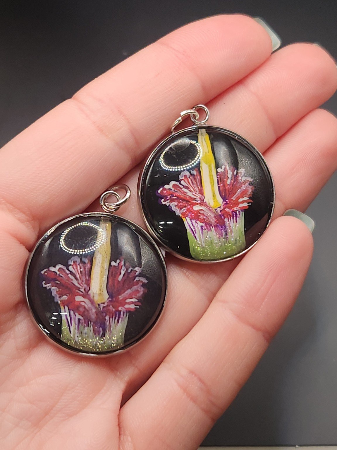 Corpse flower pendant comparison held in a hand: the hand-painted original is at the top right, and the printed reproduction is at the bottom left.
