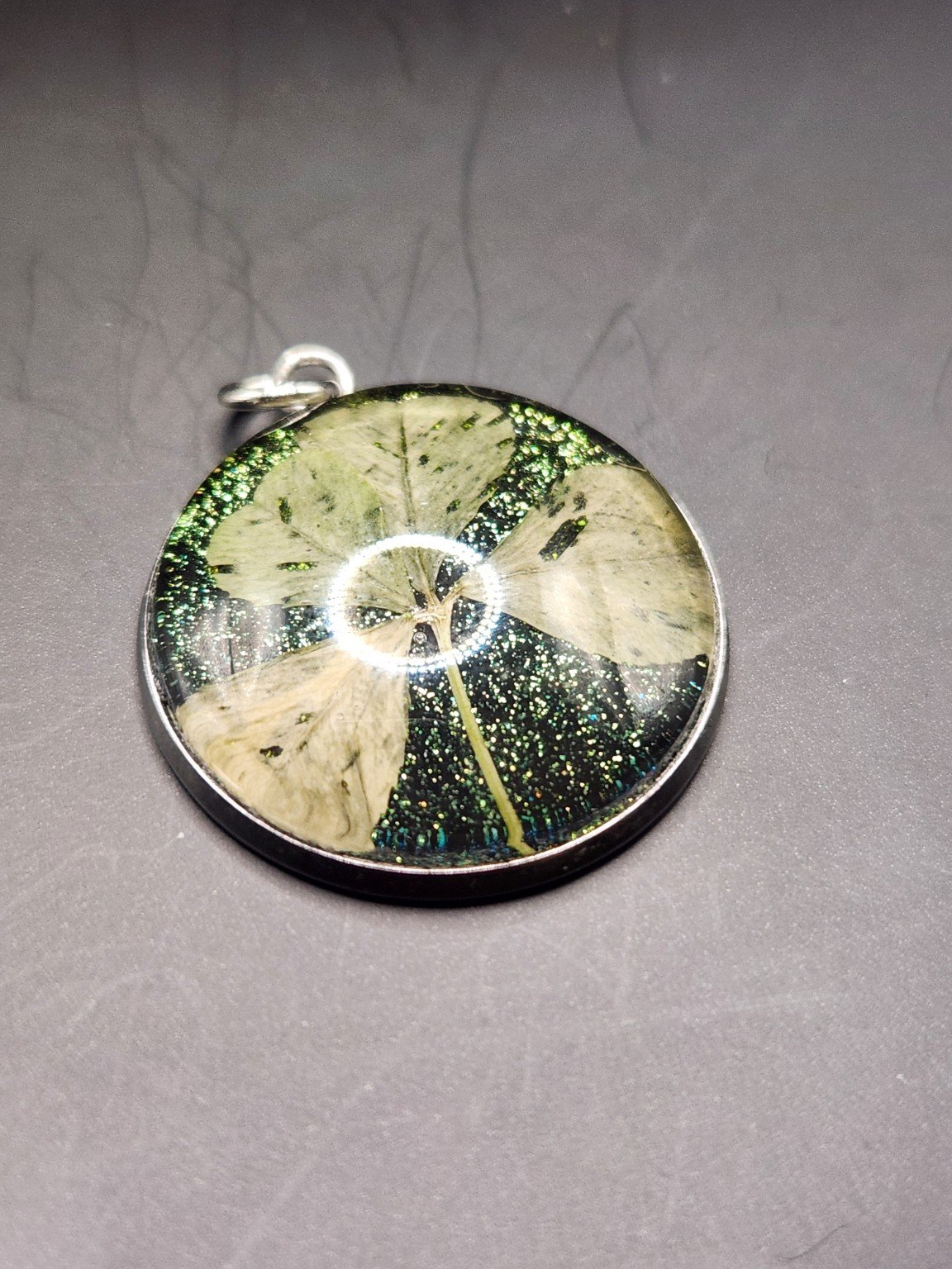 Naturally Unique N005: real pressed four-leaf clover pendant with green glitter background, close-up on gray.