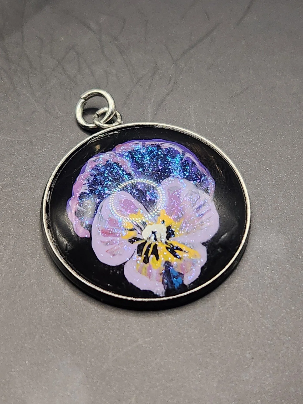 Viola flower art pendant with glitter, shown close up.