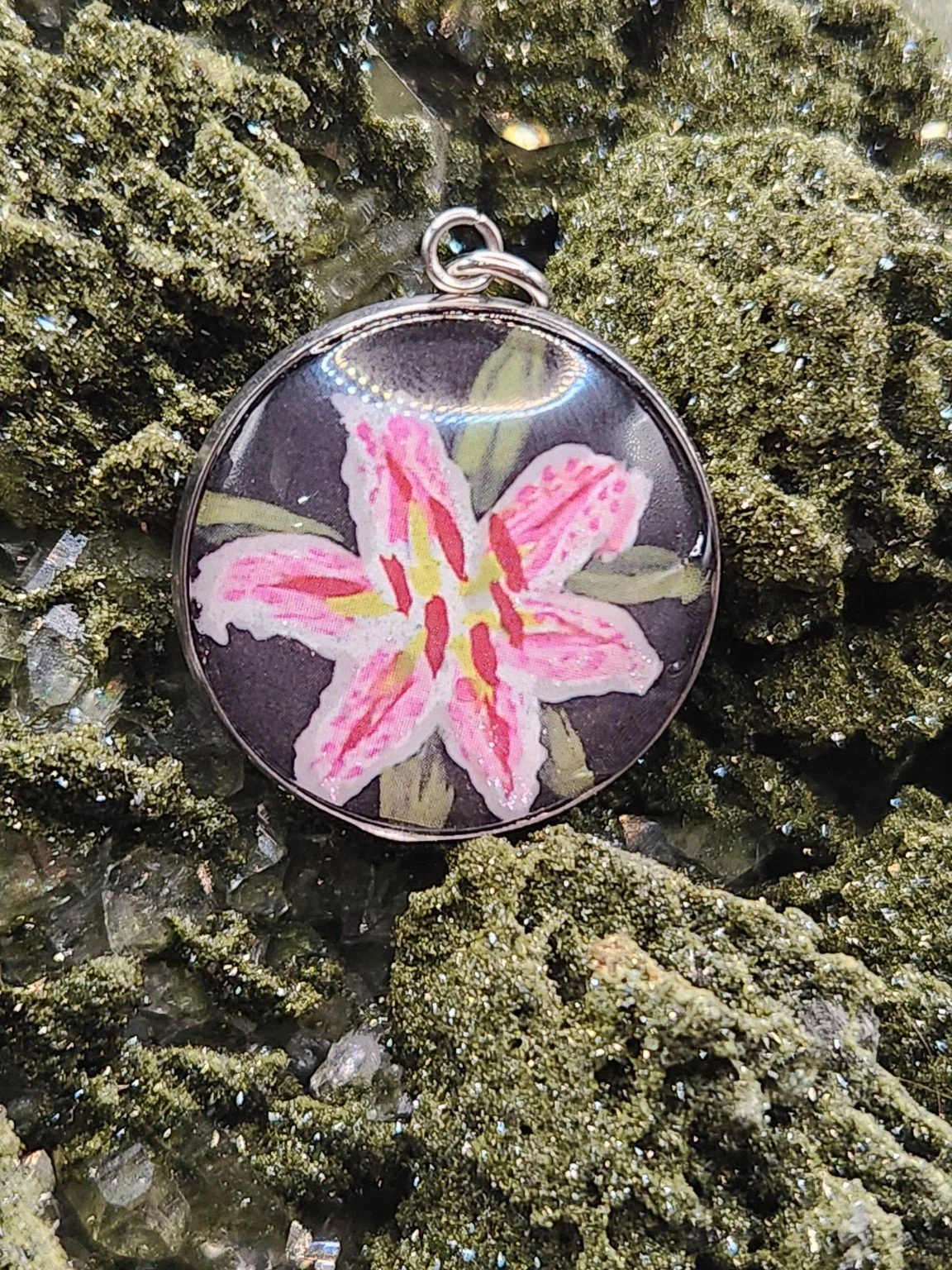 Pink-and-white Stargazer lily art pendant nestled in a sparkling green crystal display. Crystal and display props not included.